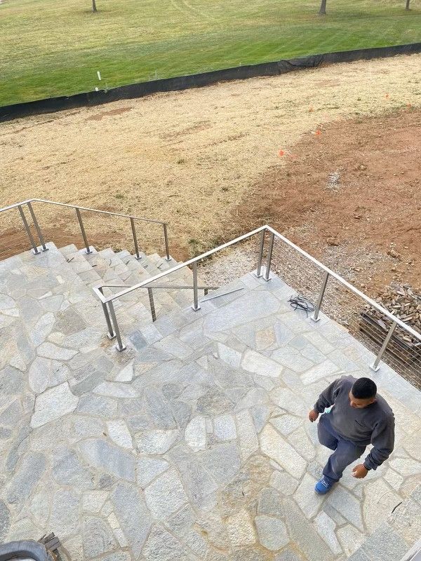A person walking down stone stairs with metal railings, near a grassy hill.