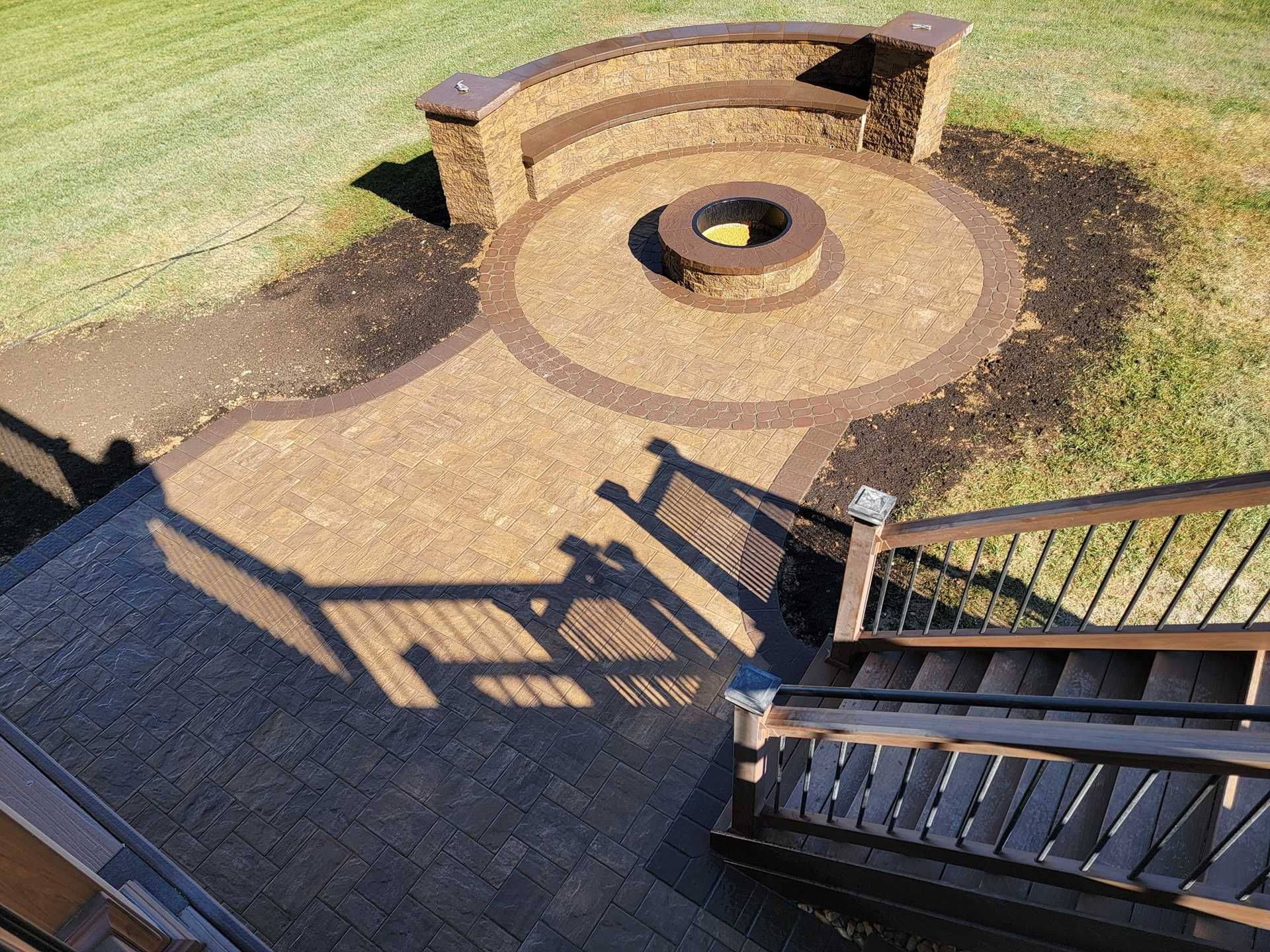 Brick patio with fire pit and seating, steps leading down, lawn in the background.