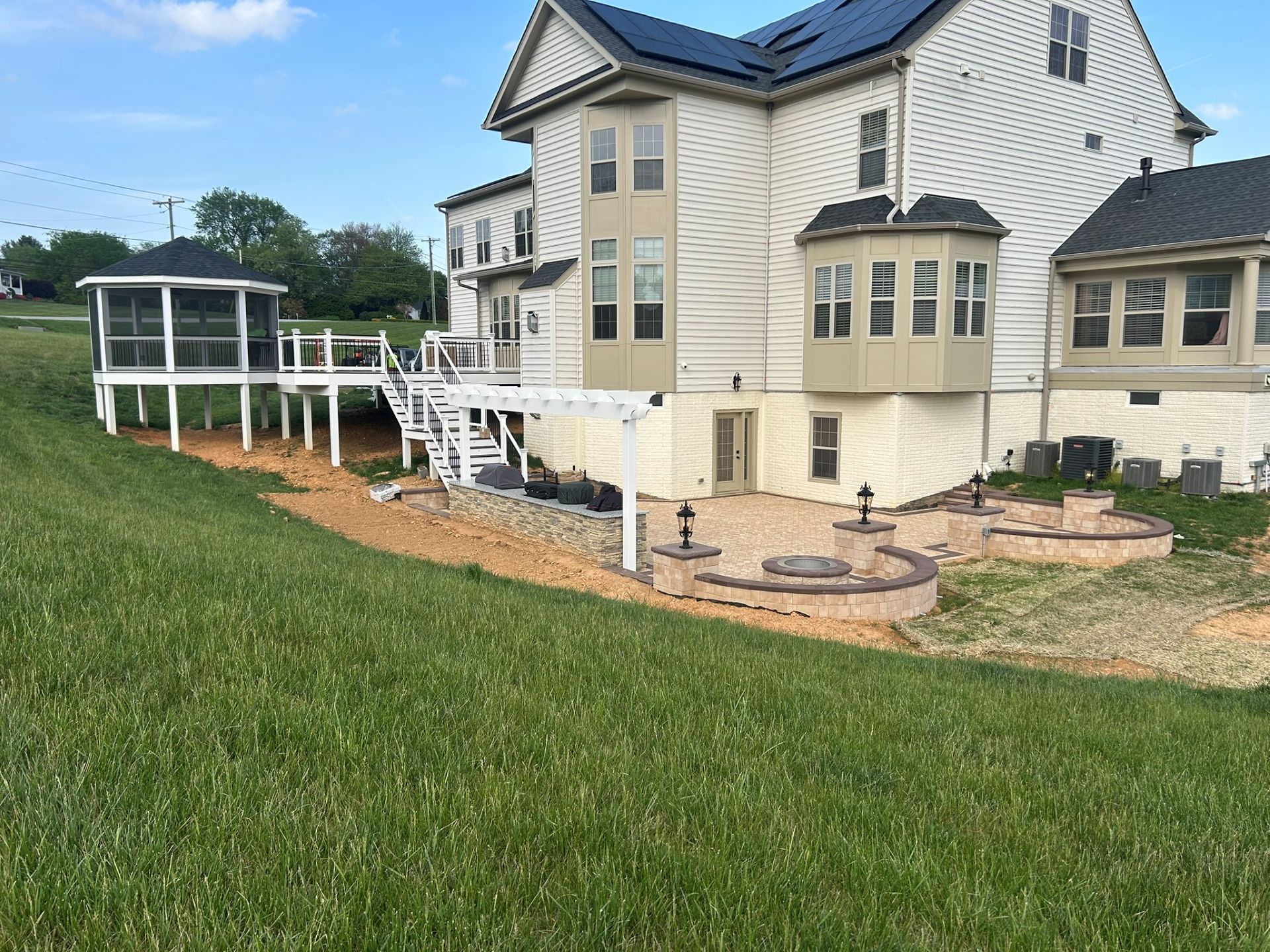 Back of a large house with a deck, screened gazebo, and patio on a grassy slope.