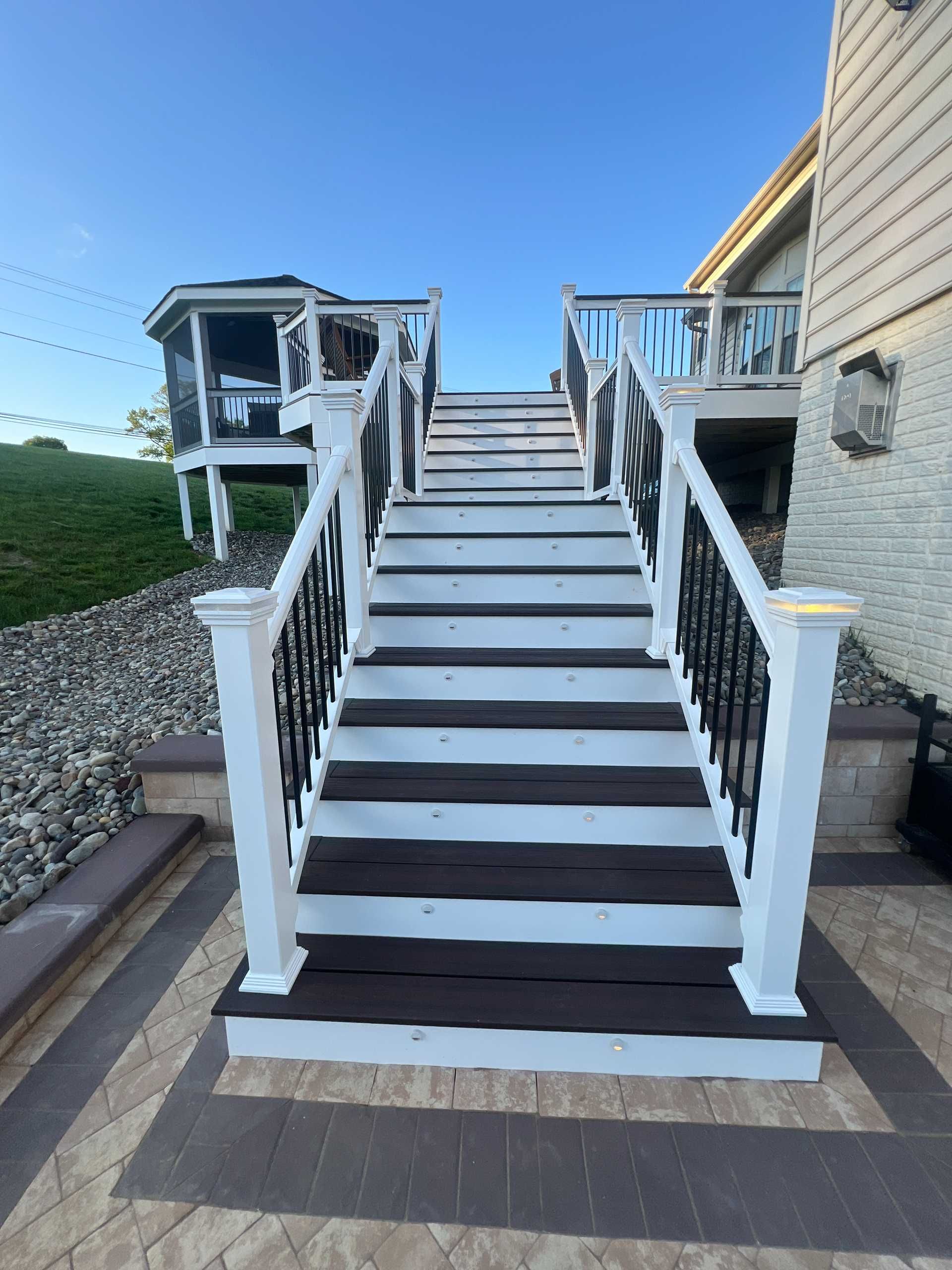 Staircase leading up to a house with a gazebo in the background. White posts, dark treads, and black railings.