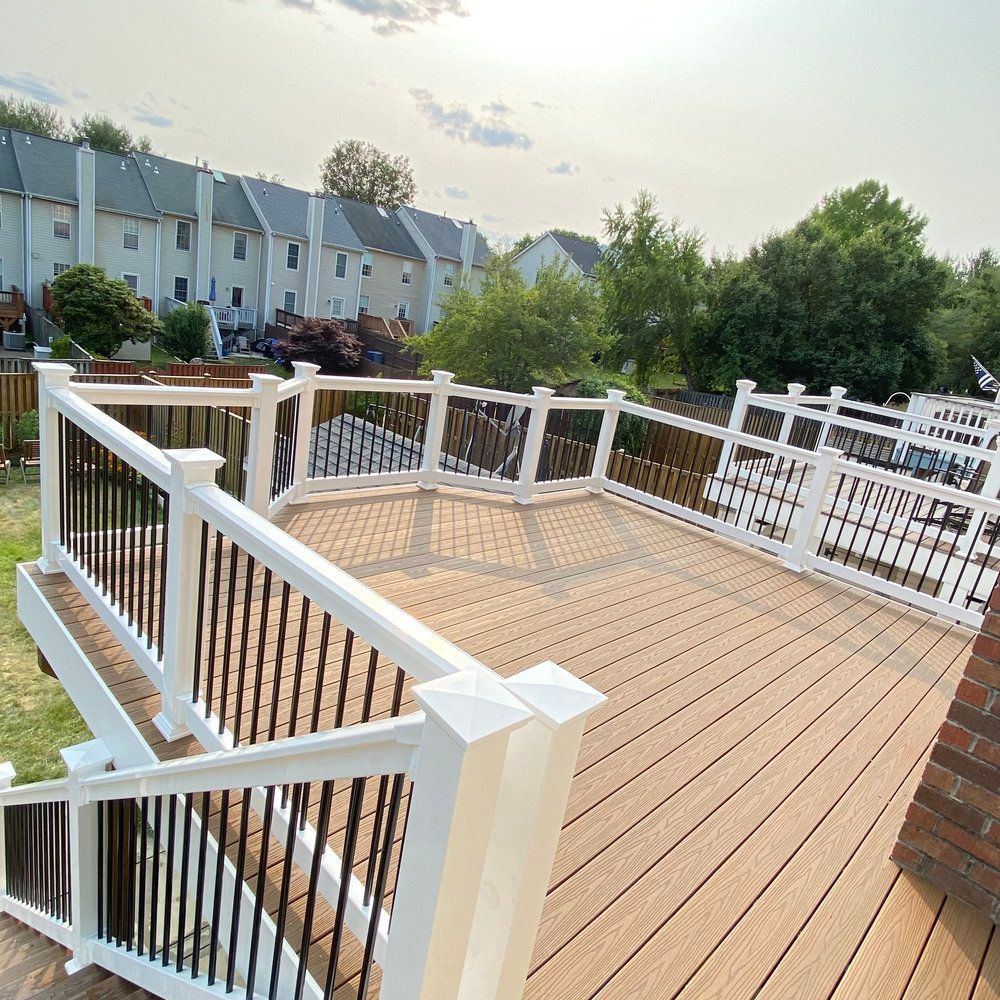Wooden deck with white and black railings, overlooking a backyard with townhouses in the background.