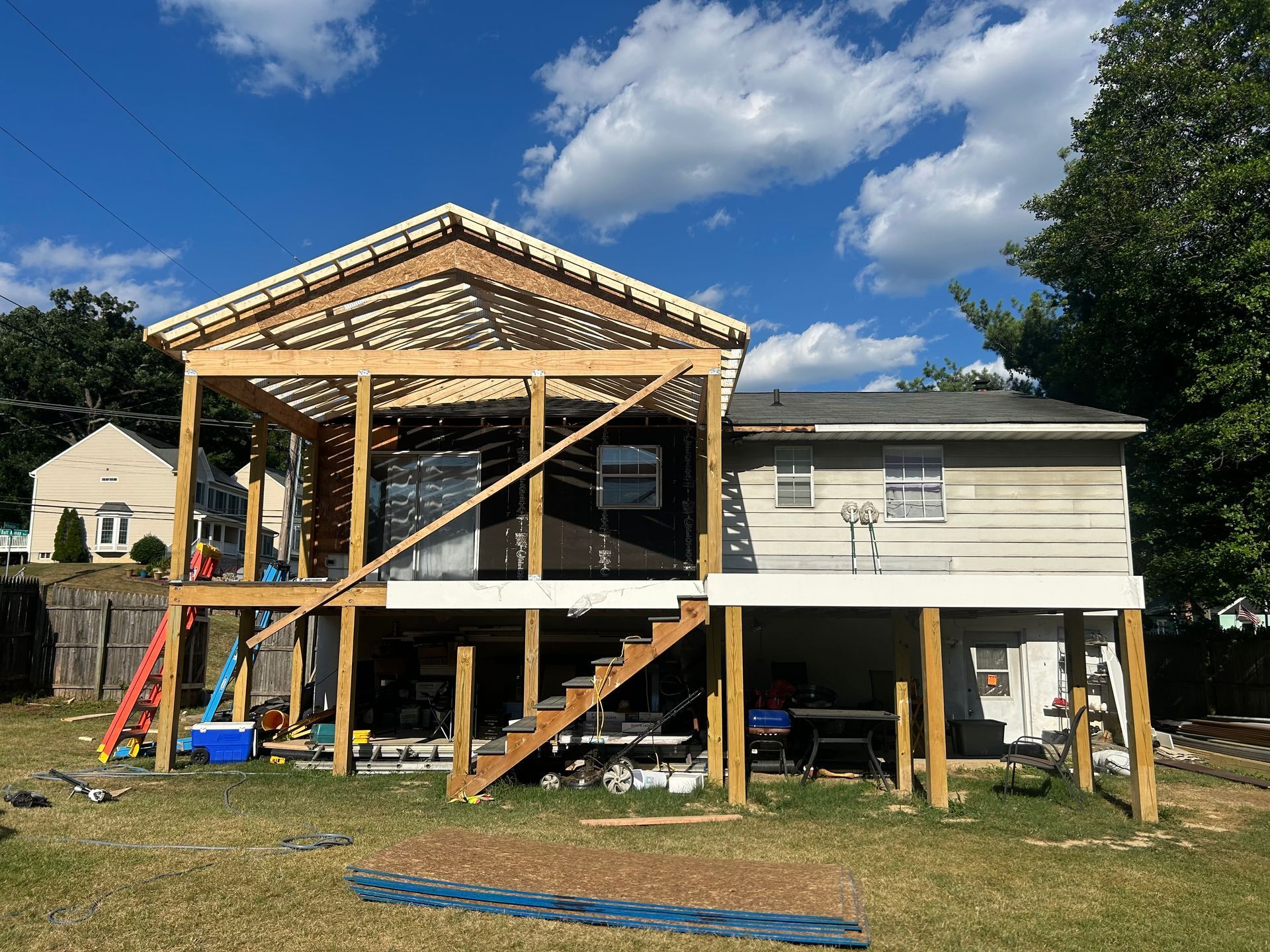 Backyard deck addition under construction with stairs, wooden beams, and blue sky.