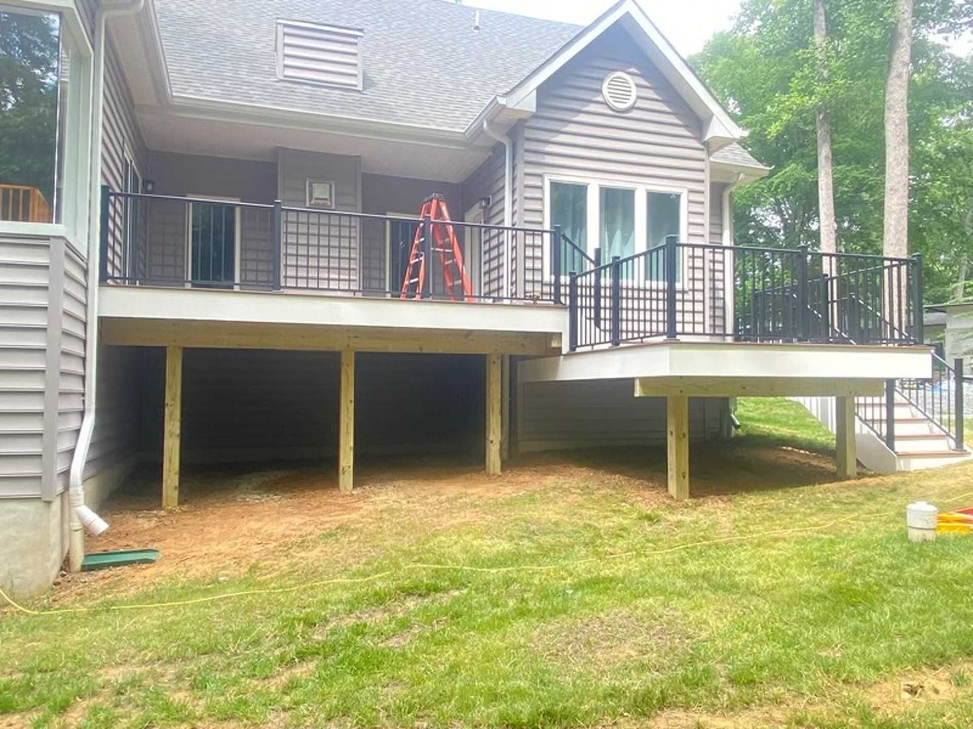 Exterior view of a house with a raised deck and black metal railings. A ladder is on the deck.