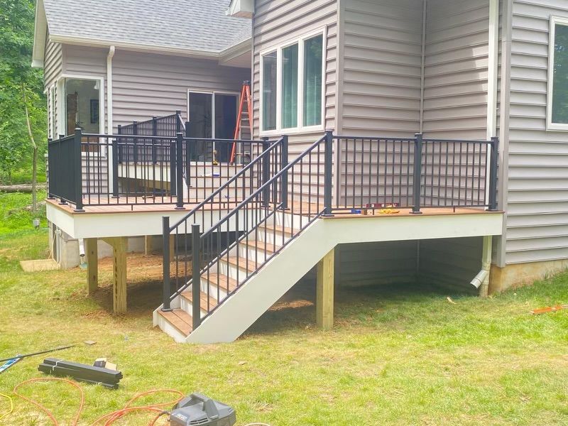New deck with black railing and stairs attached to a gray house, on green grass.