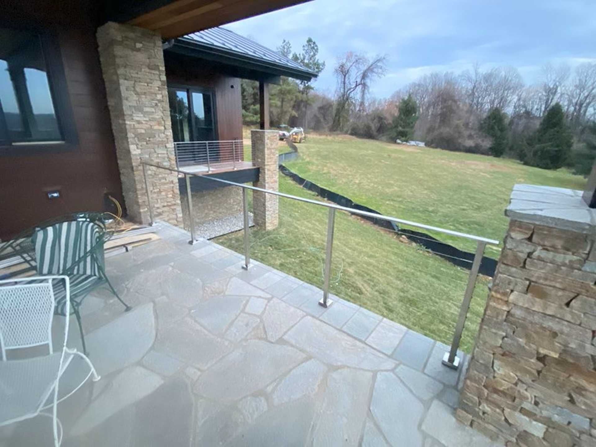 Patio with stone floor, glass railing, and grassy backyard. Brown house with stone columns.