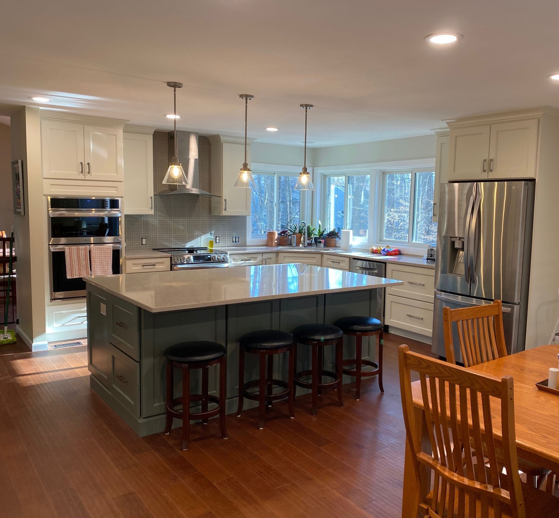Spacious kitchen with a green island, beige cabinets, and a stainless steel refrigerator.  Wooden table and bar stools.