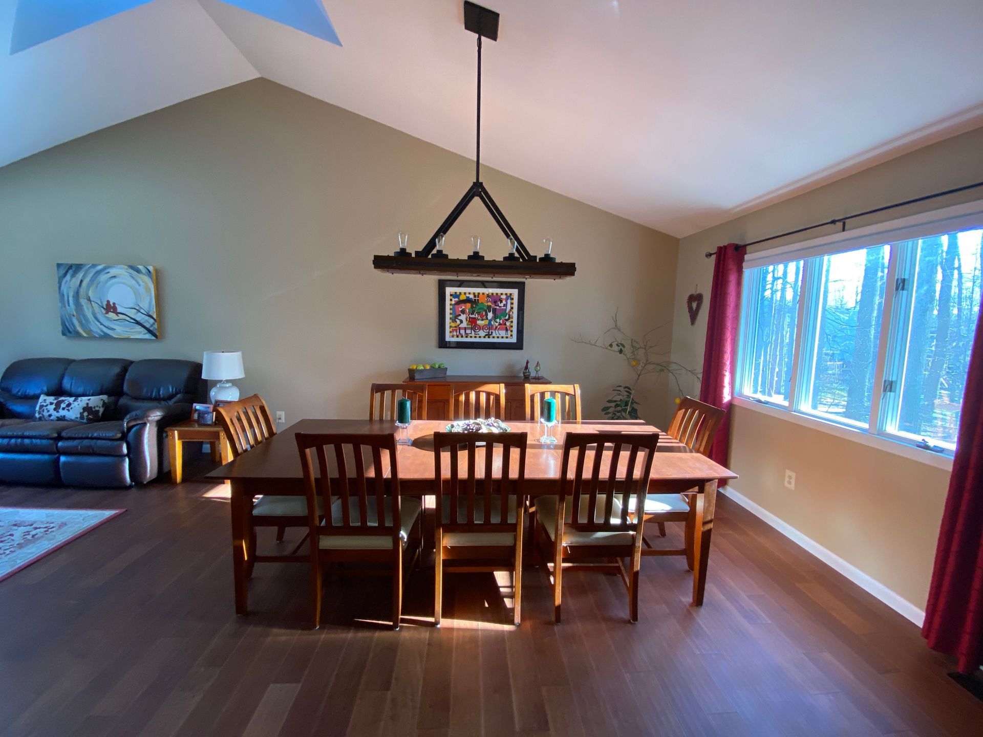 Dining room with a long wooden table and chairs, chandelier, and a sofa.
