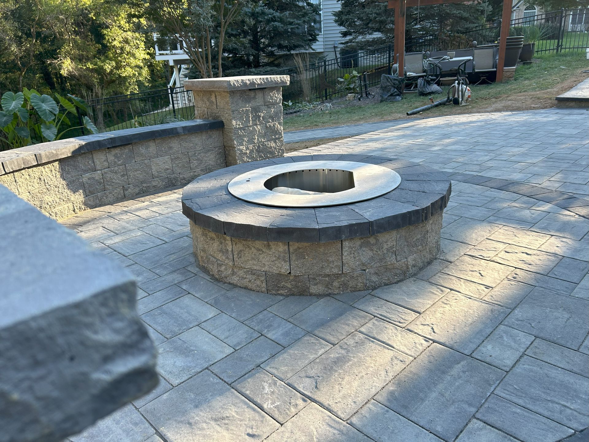 Fire pit on a stone patio with retaining wall, trees in background, sunny.
