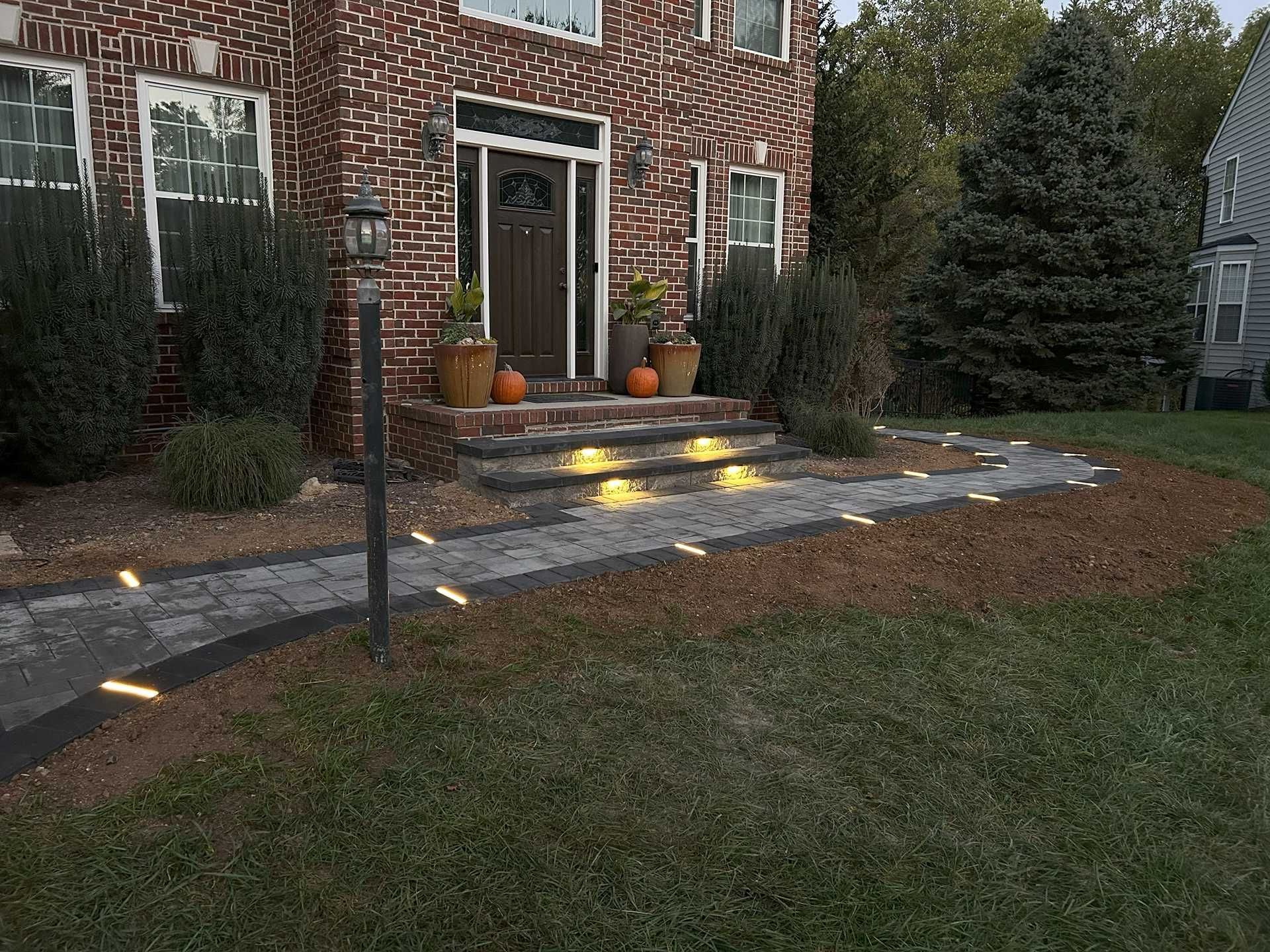Brick house with walkway lit by small ground lights leading to front door with pumpkins.