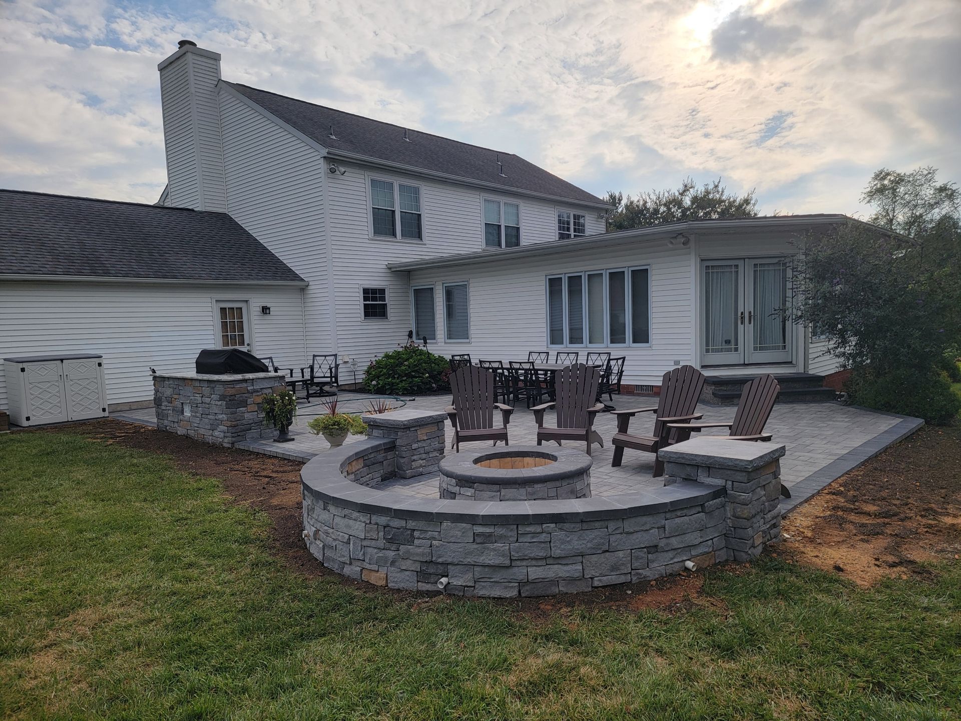 Backyard patio with fire pit, seating, and a white house.