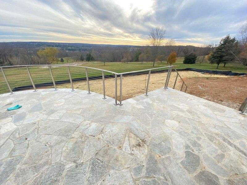 Stone patio with stainless steel railing overlooking a vast, wooded landscape under a cloudy sky.