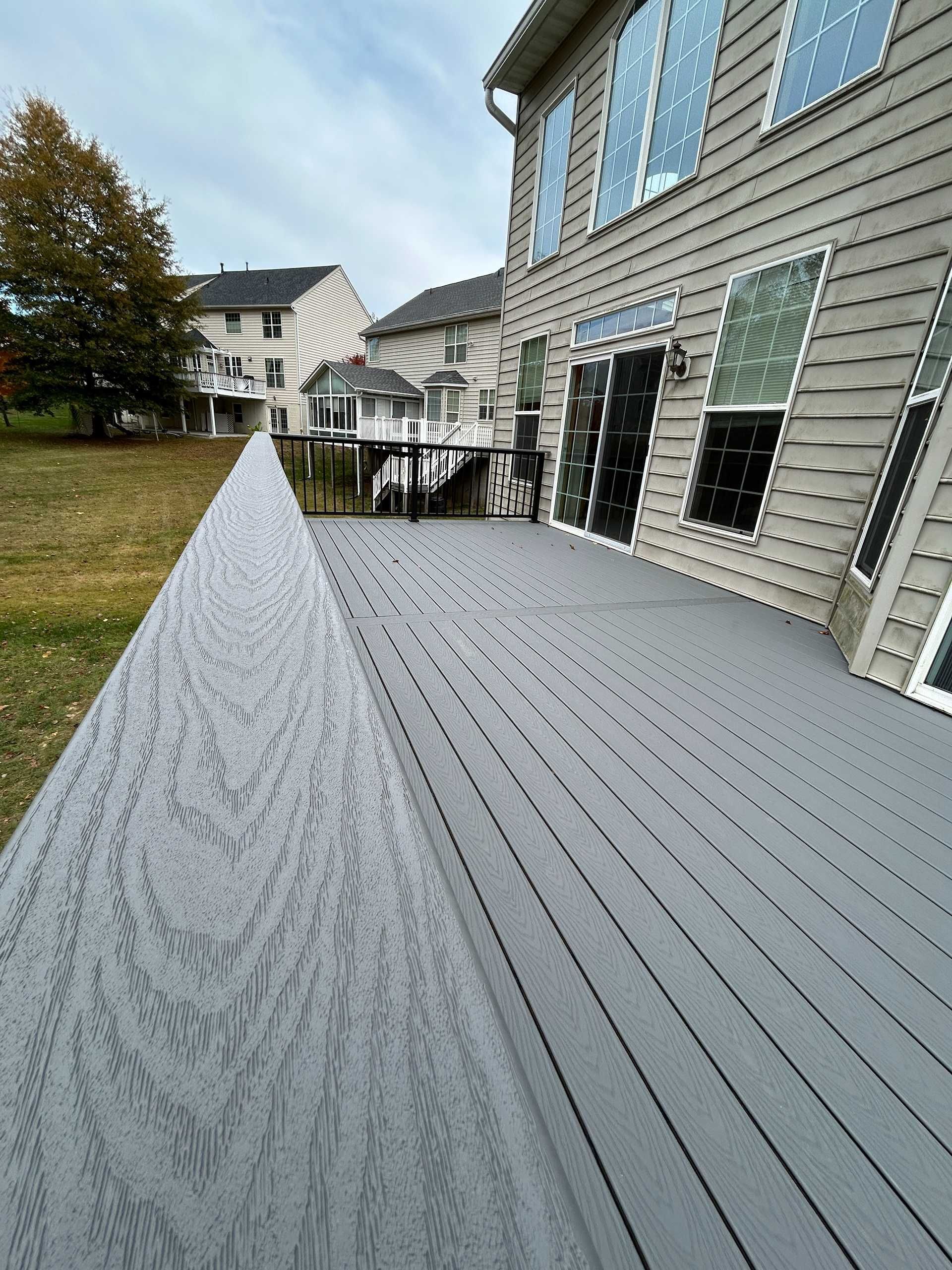 Gray composite deck next to a house with large windows, overcast day.