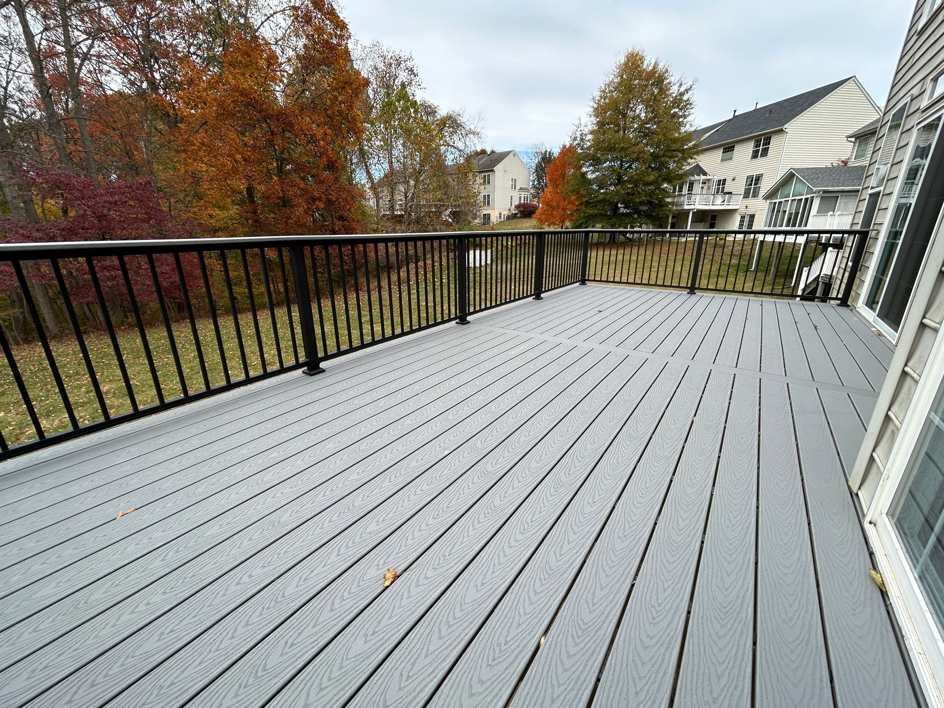 Gray composite deck with black railing overlooking a yard with trees showing fall foliage, adjacent to a house.