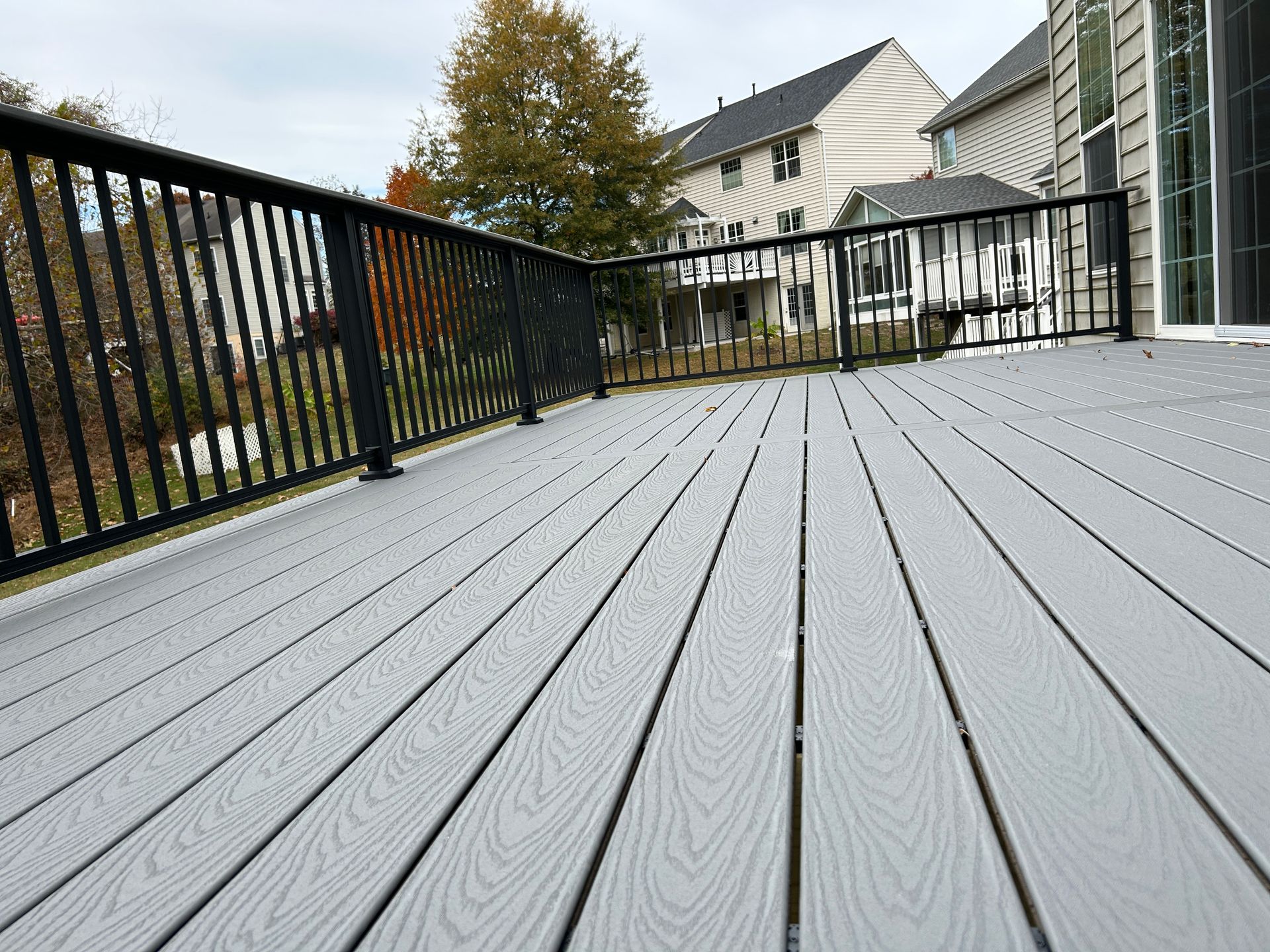 Gray composite deck with black metal railing, overlooking houses on an overcast day.