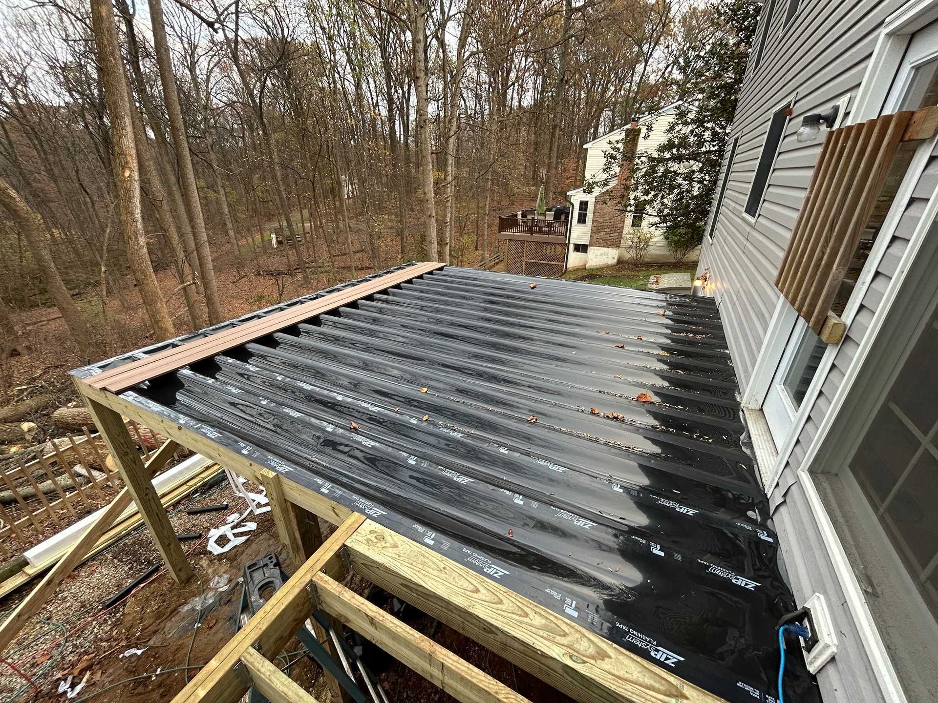 Construction of a deck roof with corrugated panels and black underlayment attached to a house.