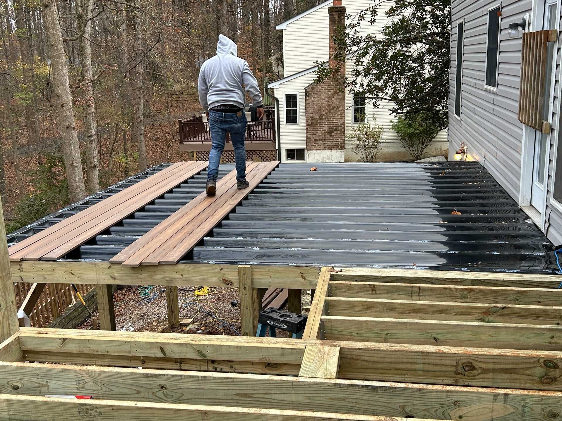 Person walking on a deck under construction, with wood planks and a house in the background.