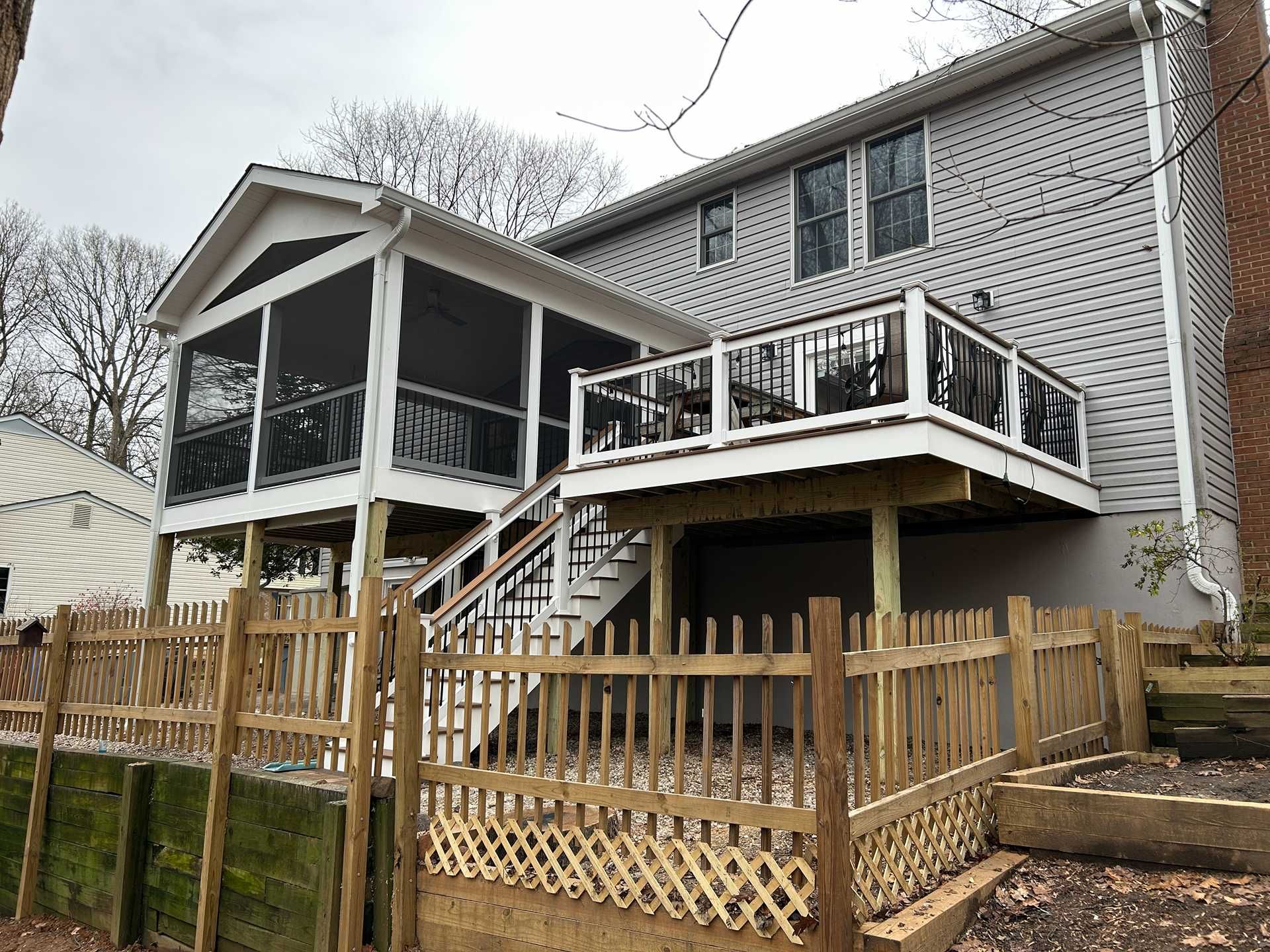 Backyard with a wooden deck, screened porch, and fence, attached to a two-story gray house.