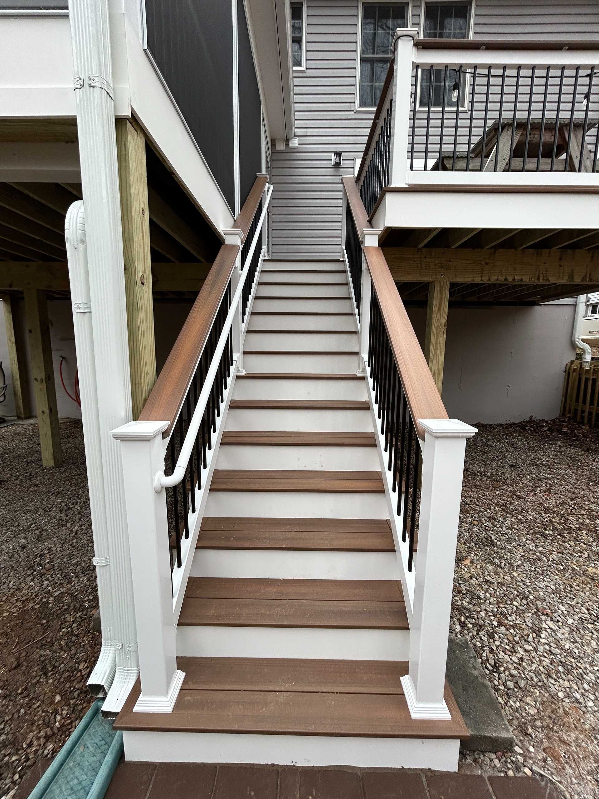 Wooden outdoor staircase with brown steps and white railings leading up to a deck.