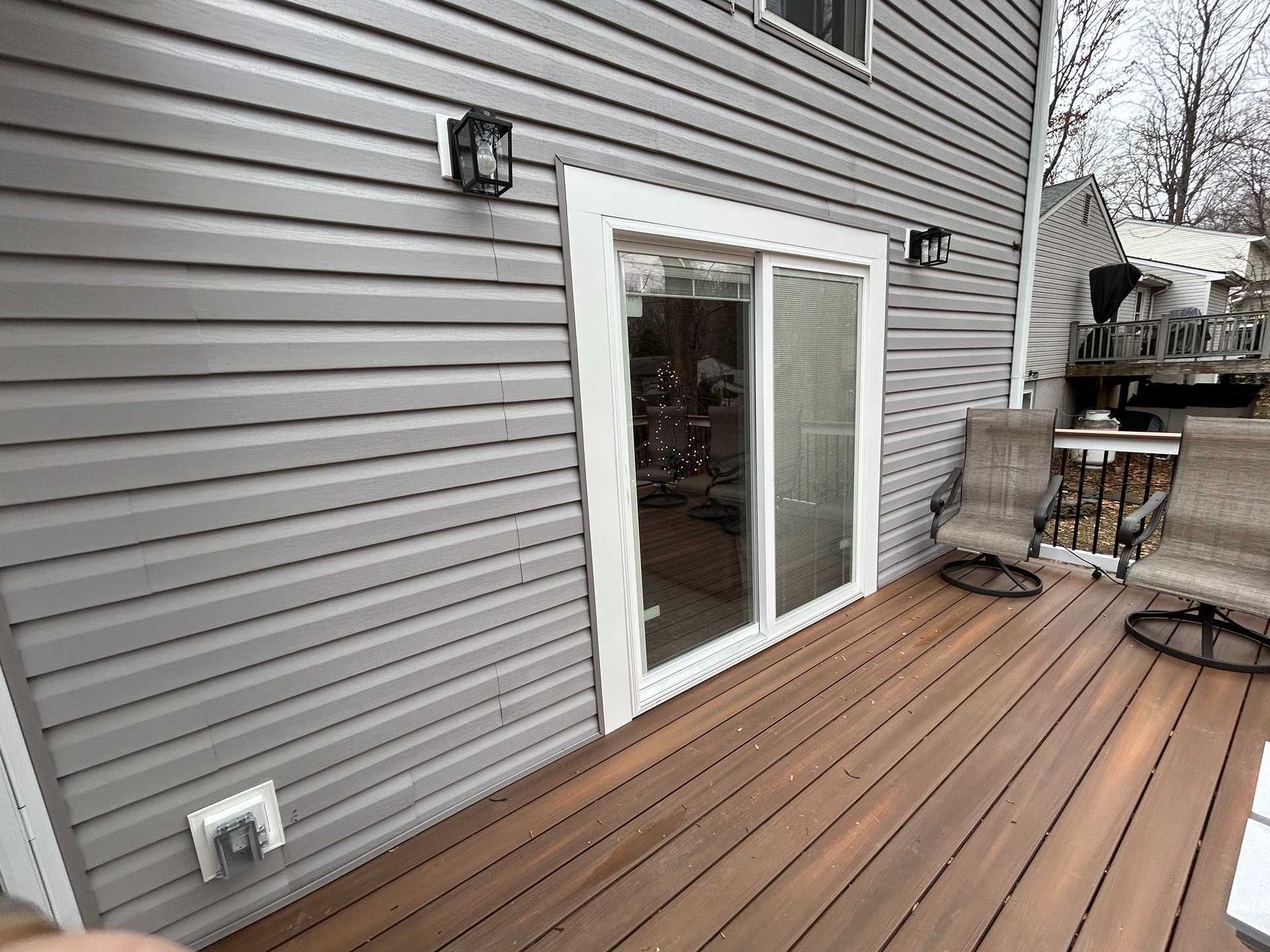 A gray vinyl-sided house with a sliding glass door and a brown wooden deck.