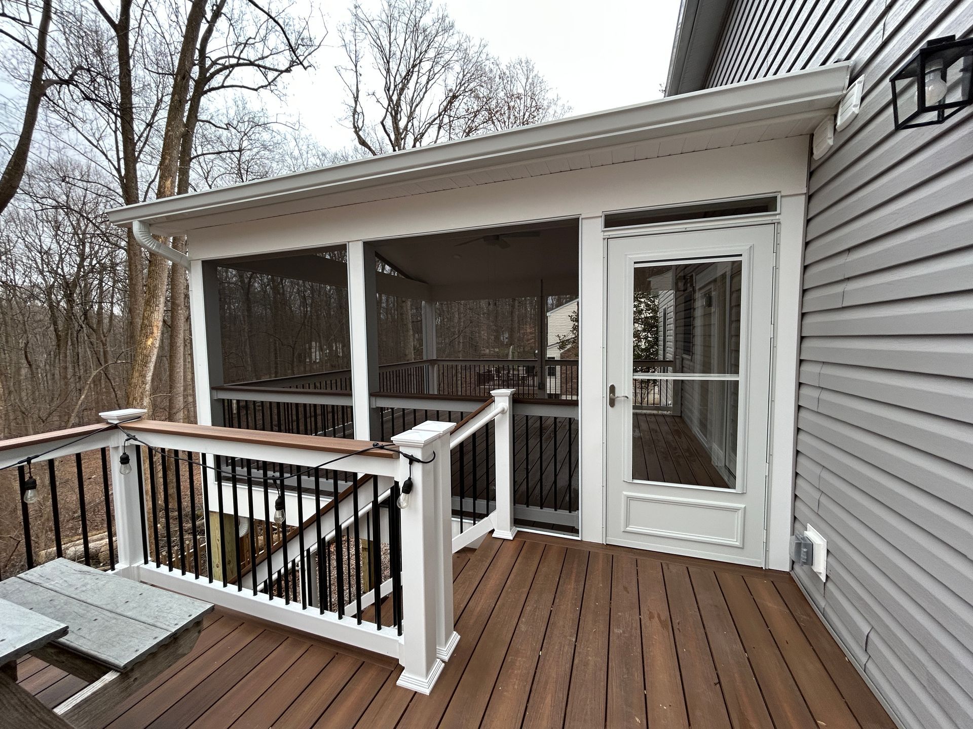 Screened porch with white trim and dark railing, next to a home with light gray siding.