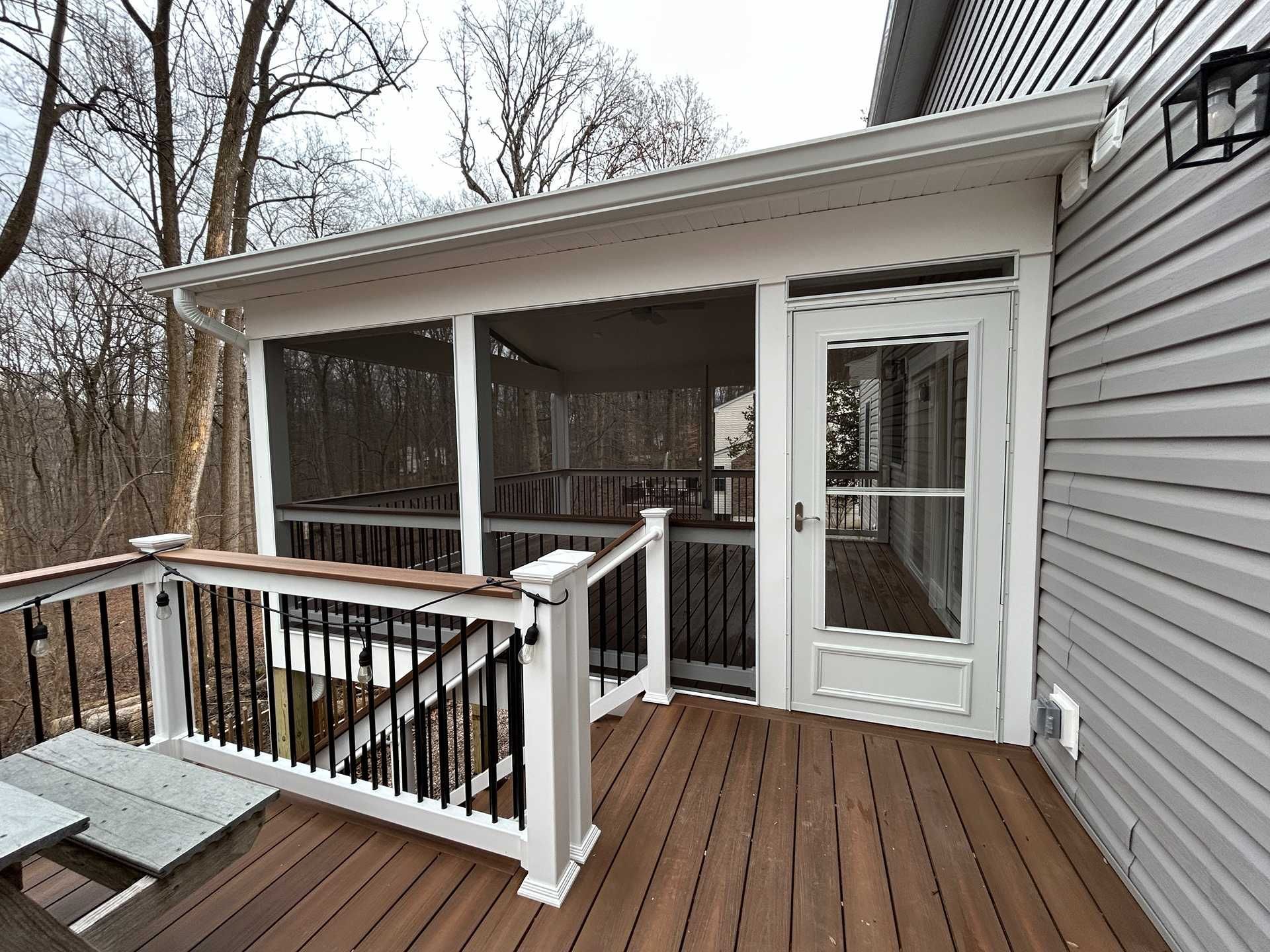 Screened porch with white trim and a brown deck, attached to a house with gray siding.