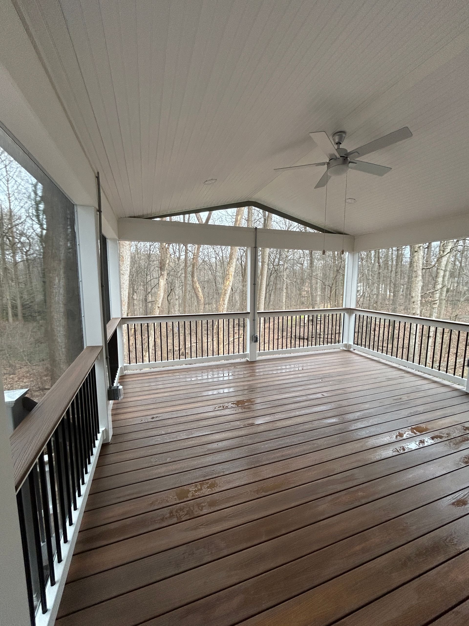Screened porch with wooden floor and railing; view of bare trees.