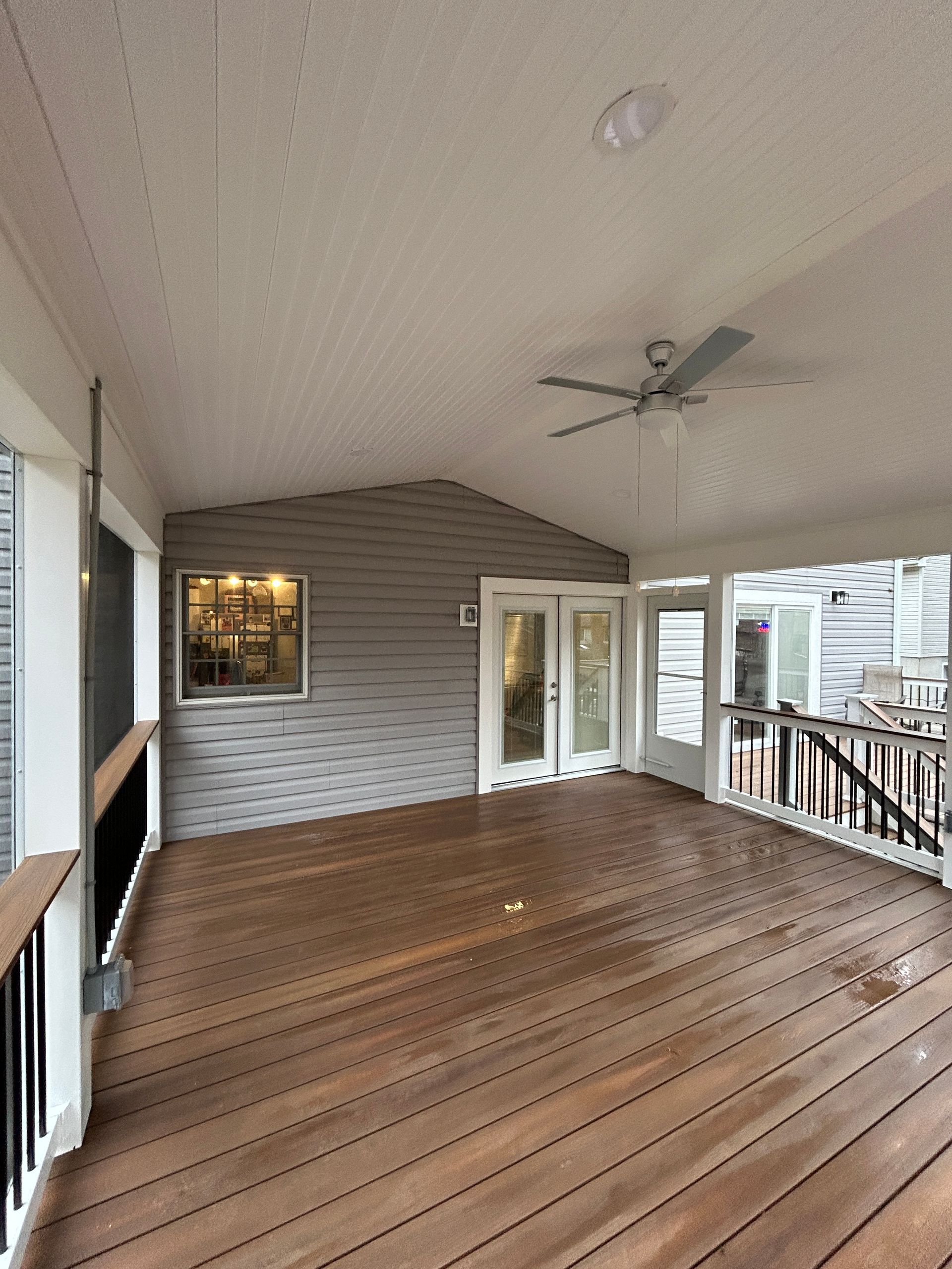Covered wooden deck with a ceiling fan, French doors, and gray siding.