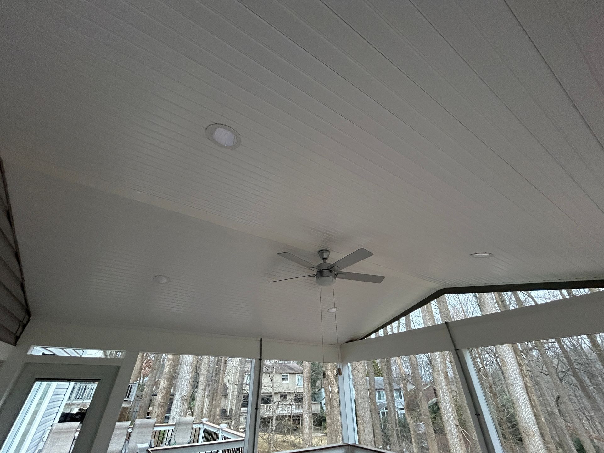 White-painted porch ceiling with a light fixture and ceiling fan; windows reveal trees and buildings outside.