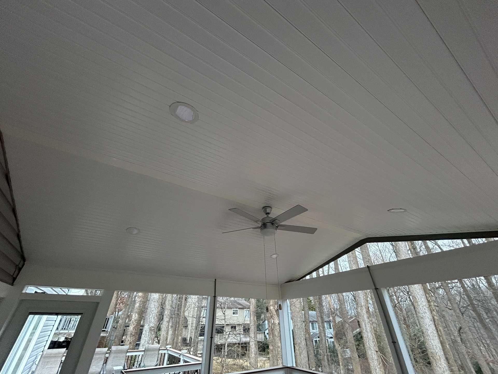 White porch ceiling with a ceiling fan and recessed lighting, overlooking a wooded view through windows.