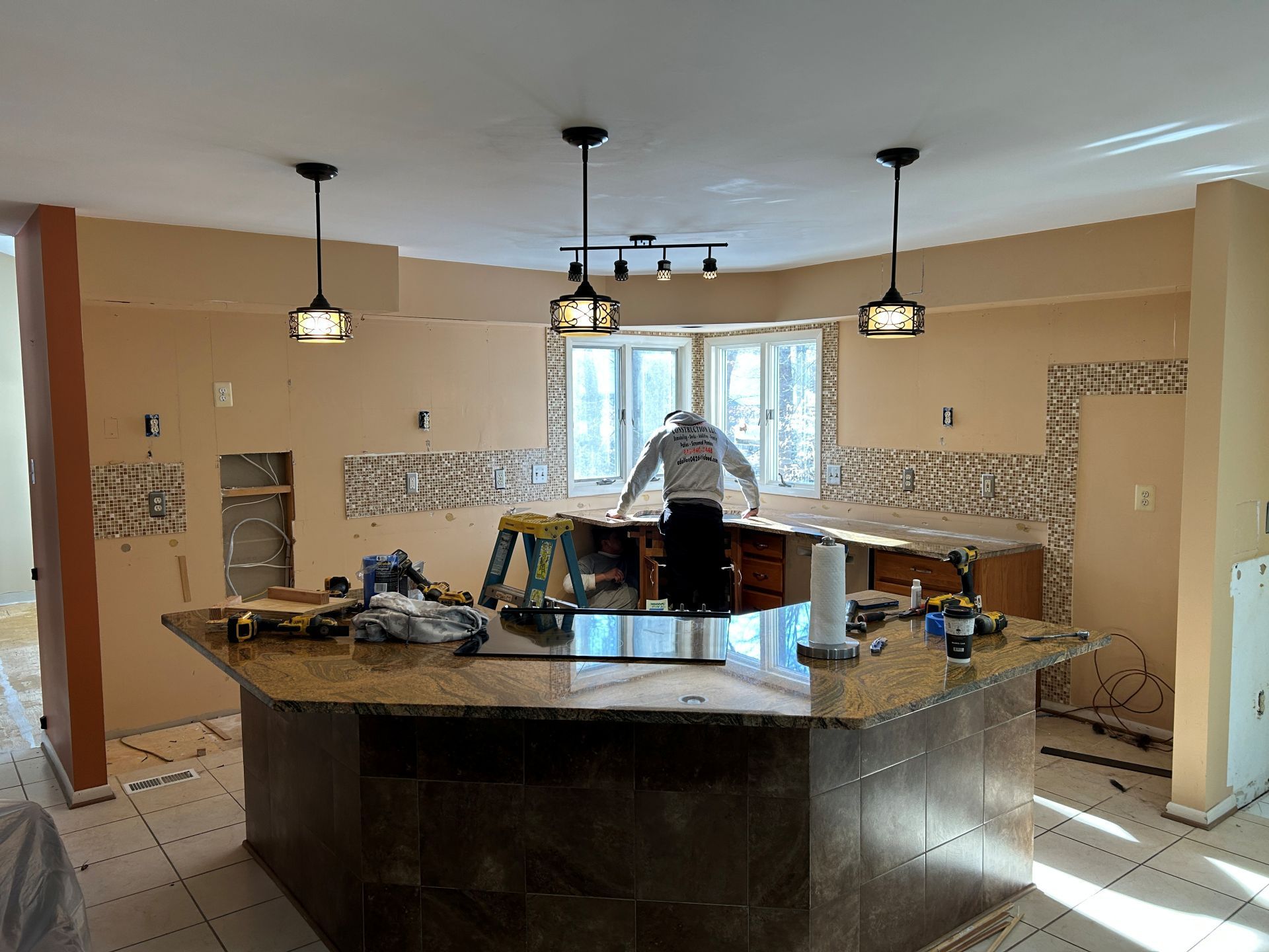Kitchen renovation in progress: A person works at the island counter surrounded by tools and exposed walls.