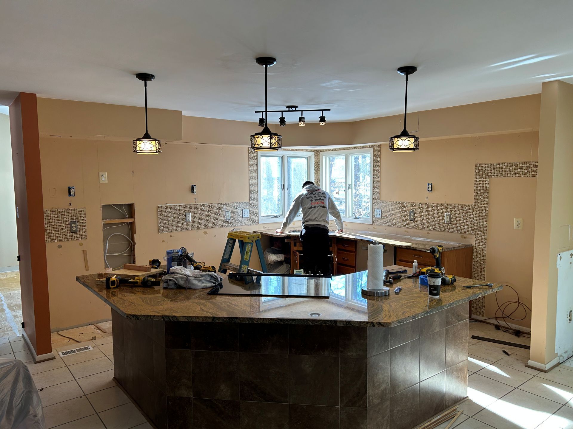 Kitchen renovation with worker at countertop, three pendant lights, backsplash tiling, and island.