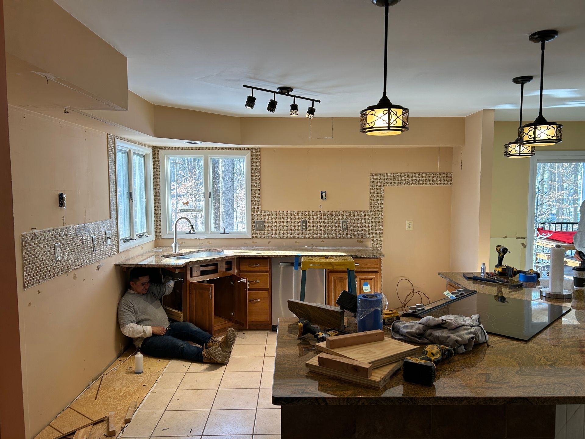 Kitchen renovation in progress: person resting near cabinets, walls partially tiled, tools on island.