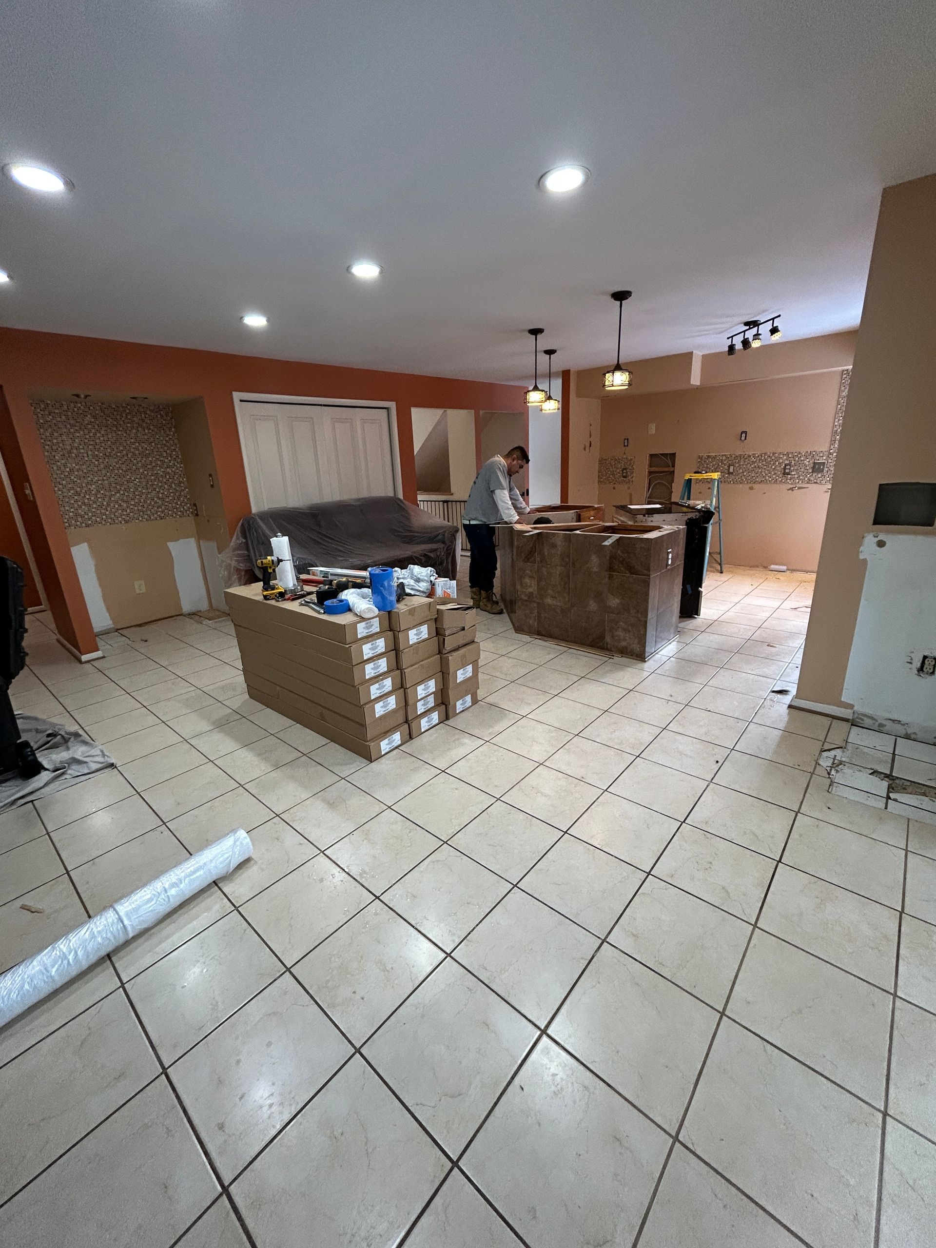Kitchen remodel in progress: boxes, cabinets, flooring, and two people working in the space.