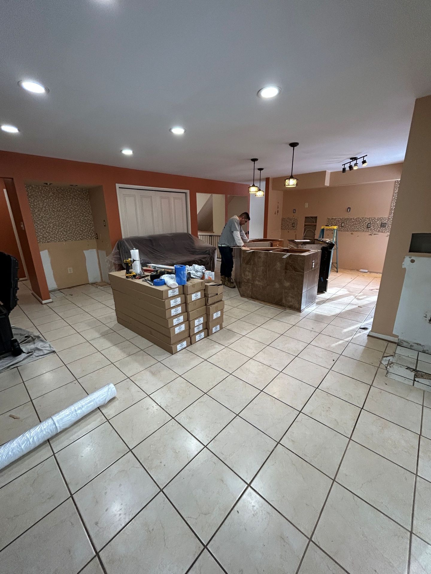 Kitchen remodel in progress with boxes, island, and tile flooring. A person stands near the island.