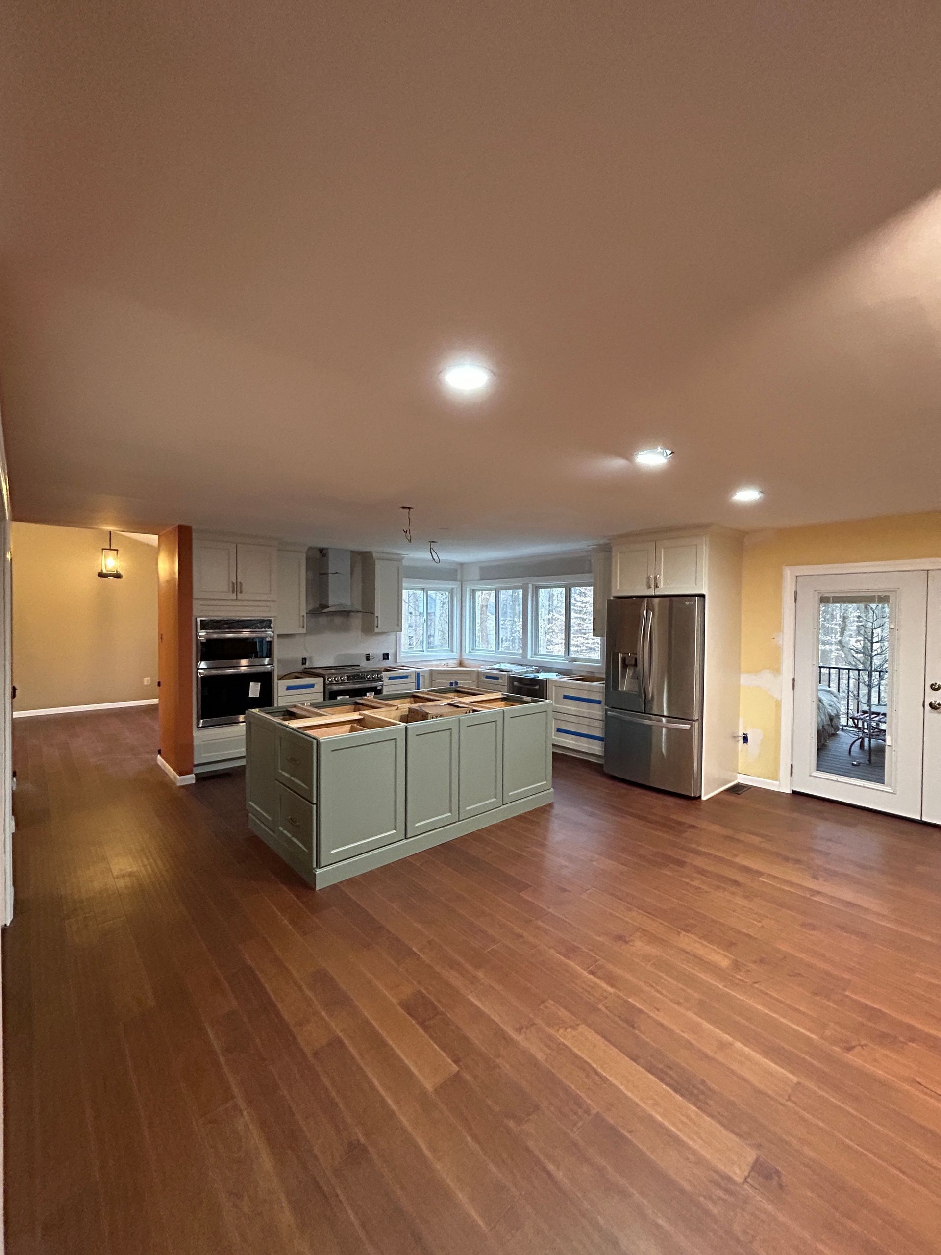 Spacious kitchen with a green island, light-colored cabinets, stainless steel appliances, and wood flooring.