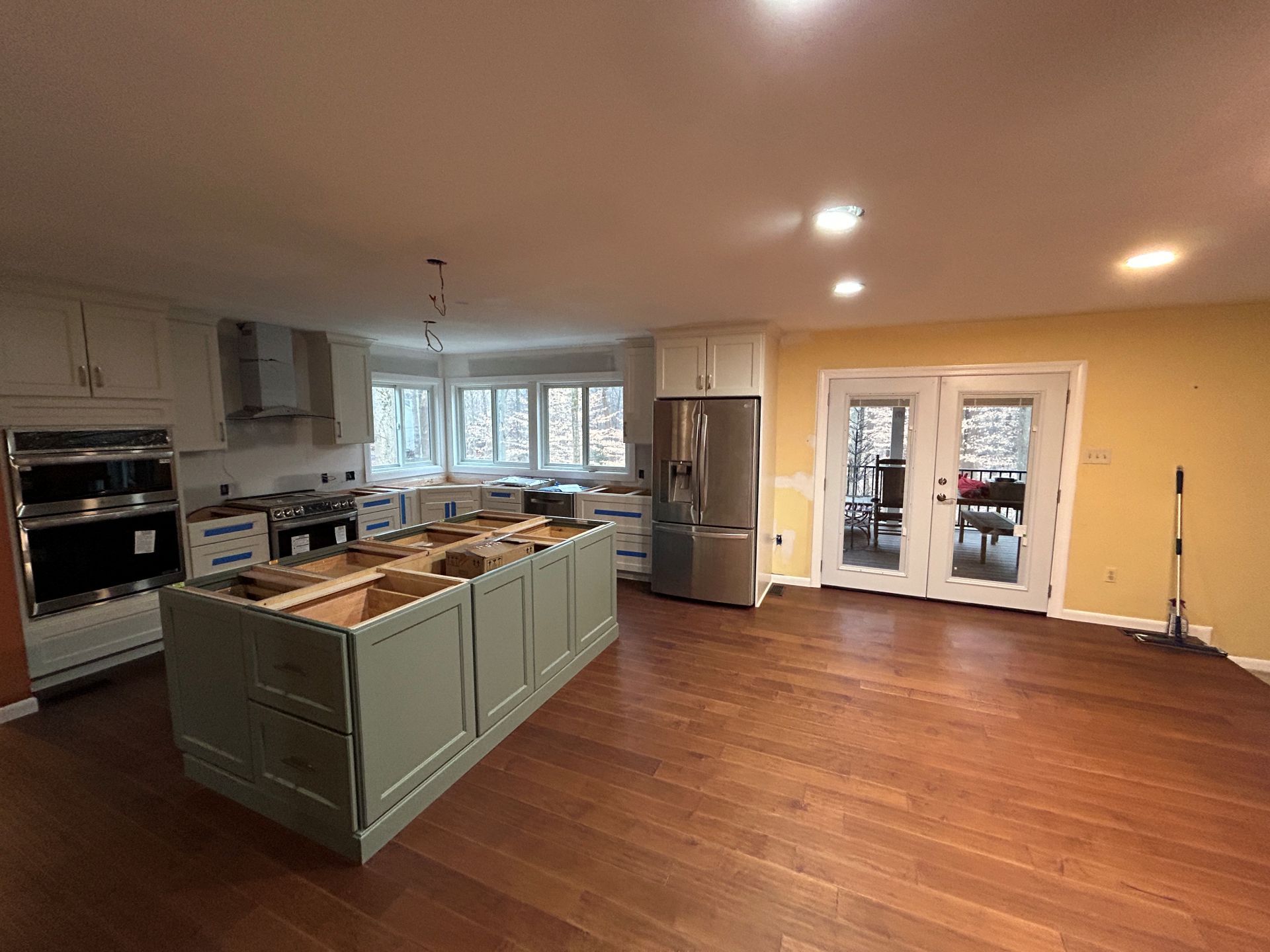 Kitchen renovation in progress, featuring a green island, light cabinets, stainless steel appliances, and French doors.