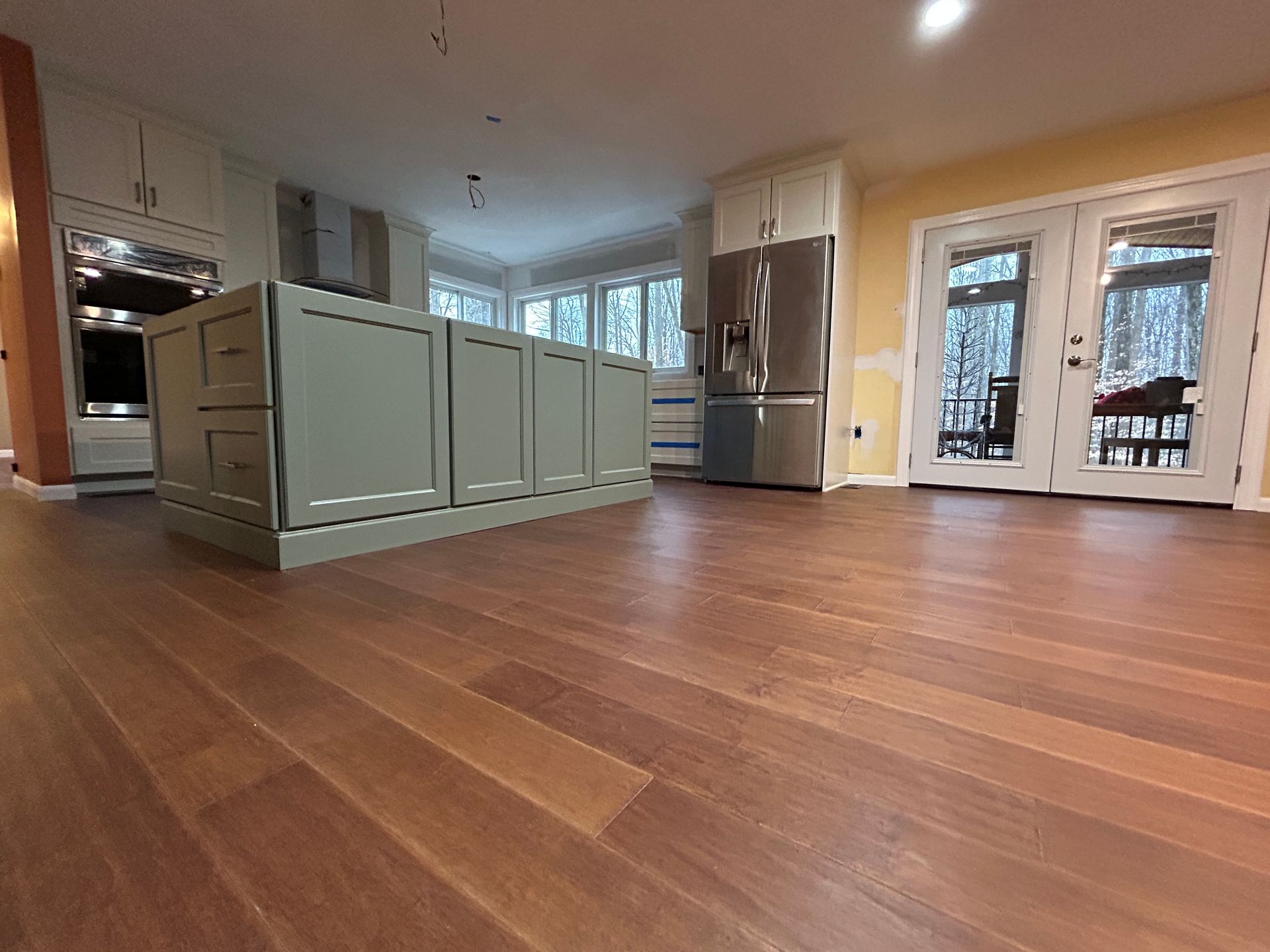Kitchen with hardwood floor, green island, stainless steel refrigerator, white cabinets, and French doors.