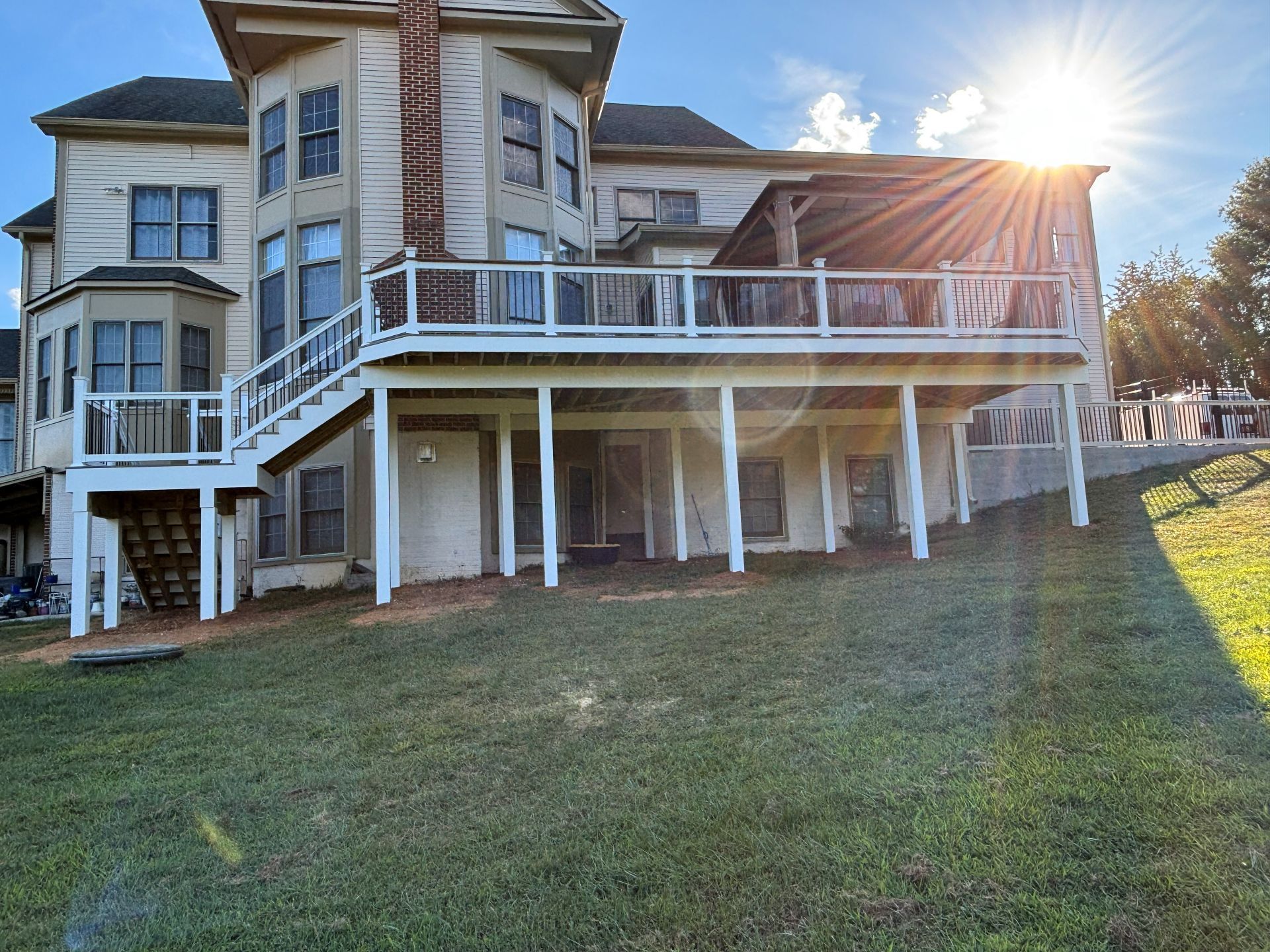 Multi-story house with a large deck, set on a grassy hill; sun shining brightly.