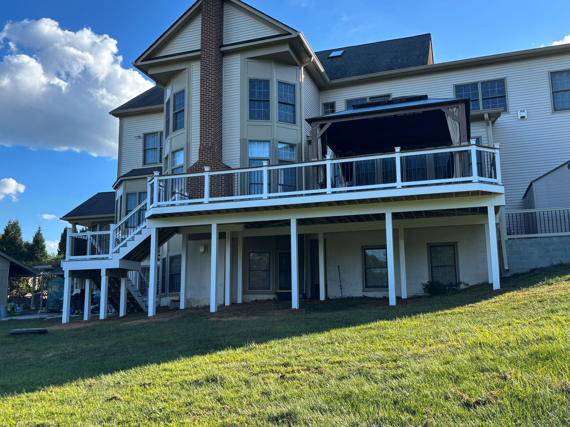 Two-story house with multi-level deck and gazebo on a grassy hillside.