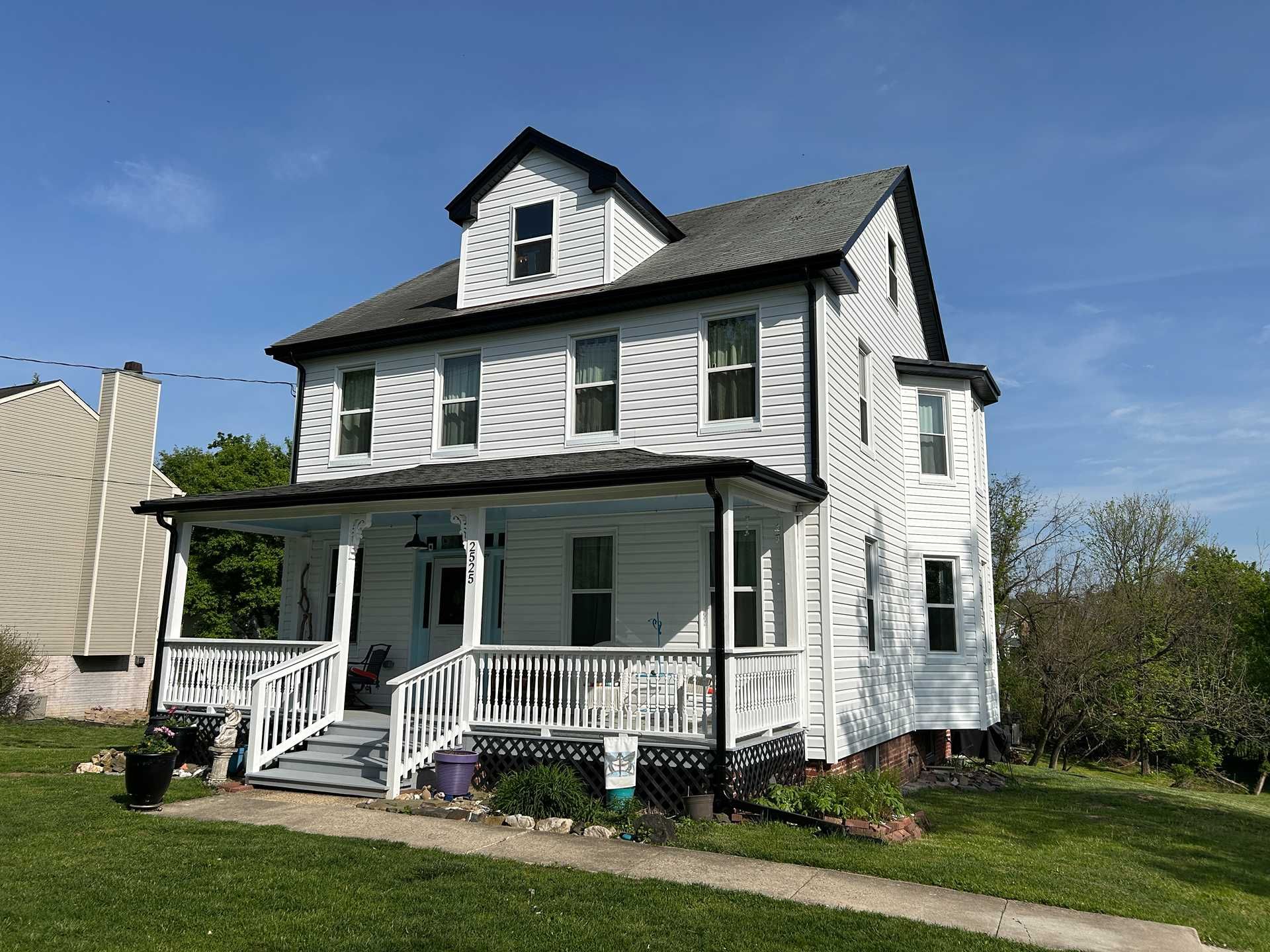 White two-story house with black trim, porch, and a dormer against a blue sky.