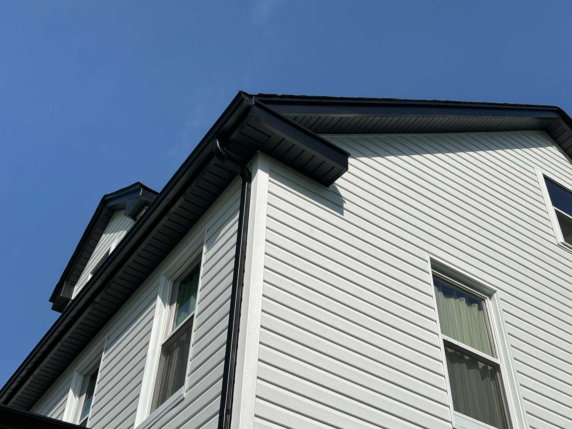 Two-story house with white siding and black gutters against a blue sky.