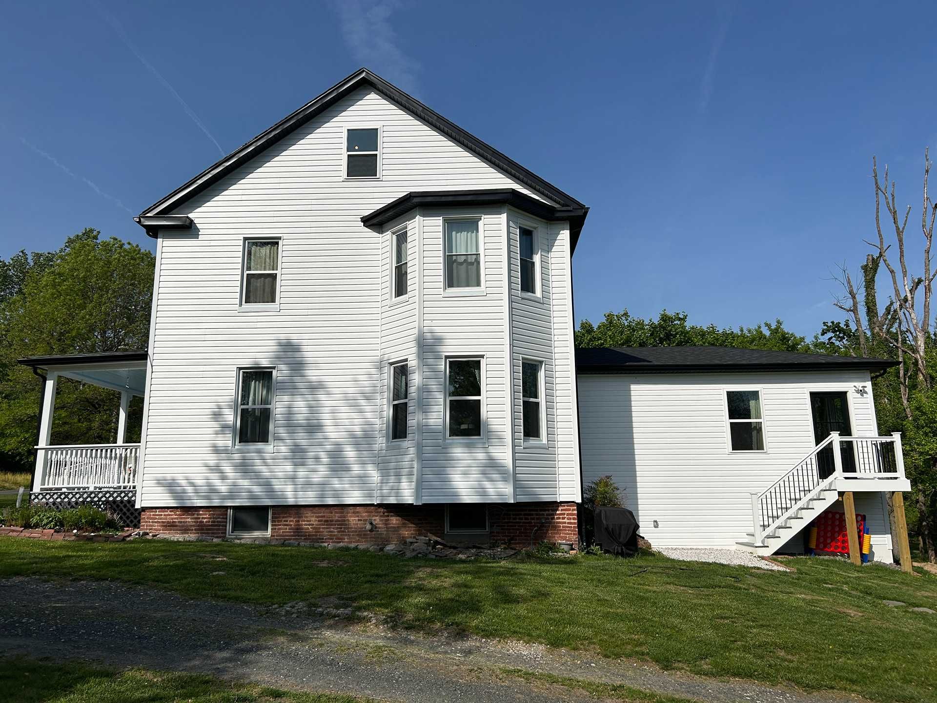 White two-story house with black roof, bay window, and small porch against a blue sky.