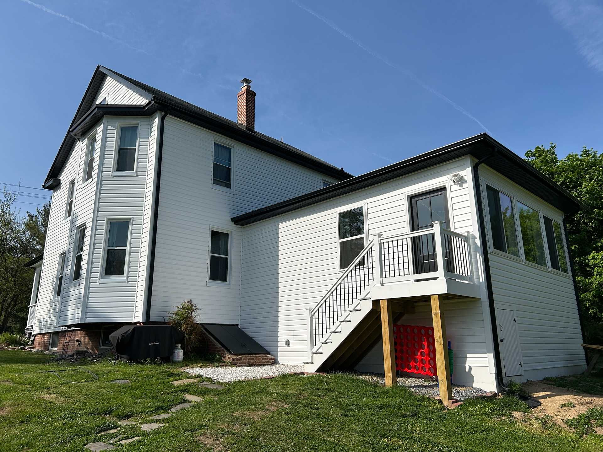White house with dark roof and trim, green lawn, exterior stairs leading to a red door.