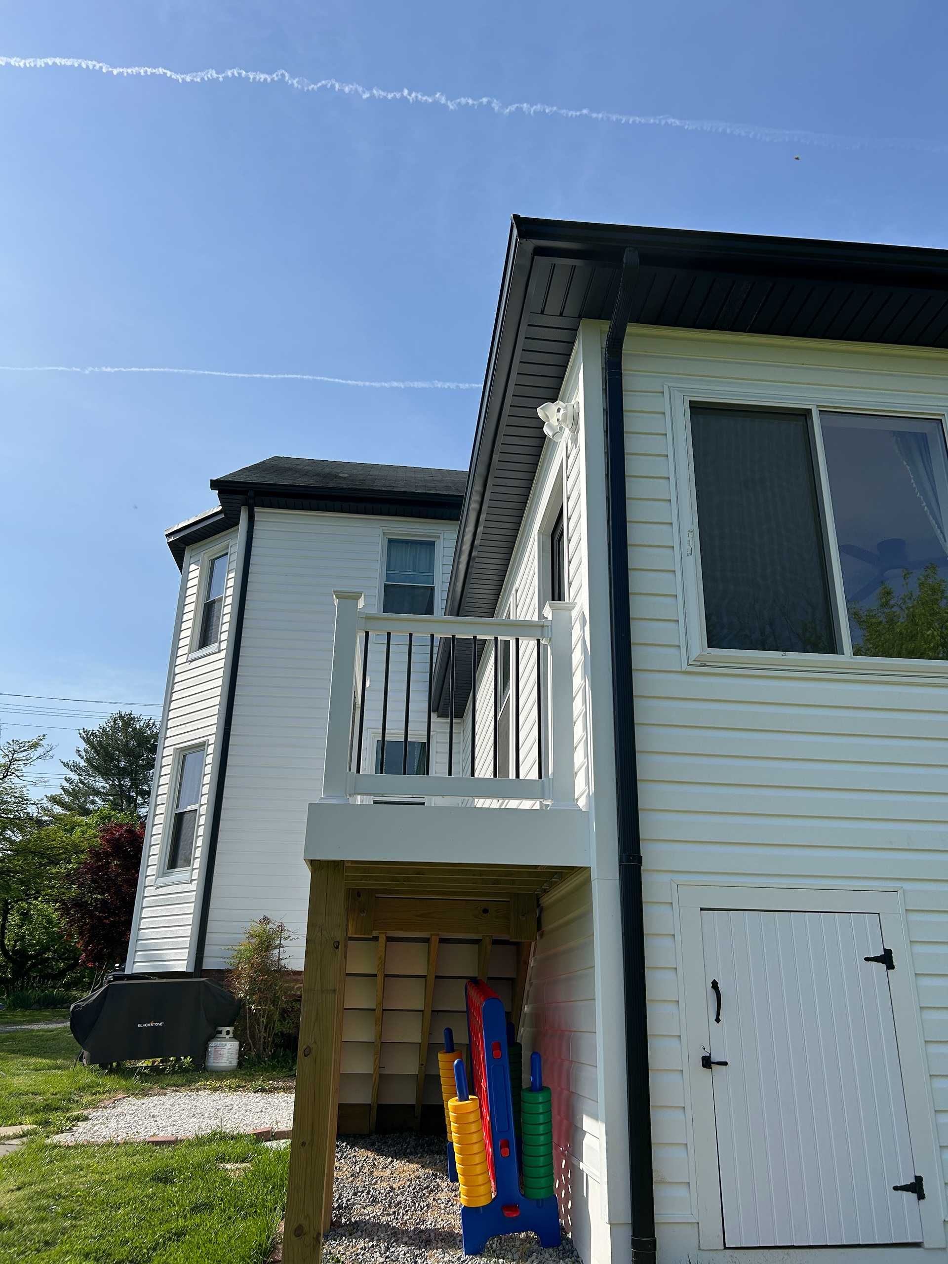White house with a small deck and colorful toys underneath; blue sky with contrails.