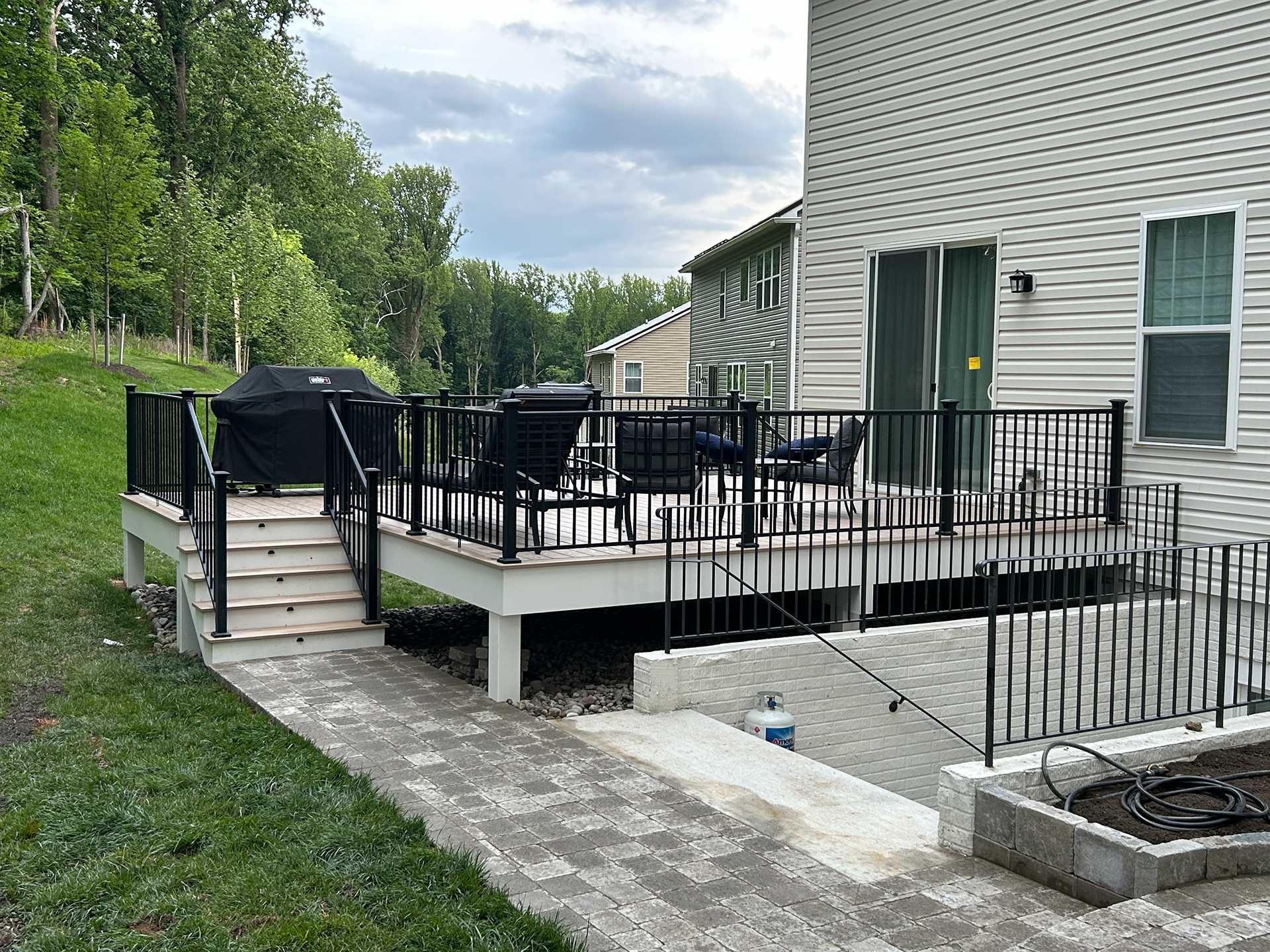 Deck with black railing, stairs, grill, and patio furniture next to a house with gray siding.