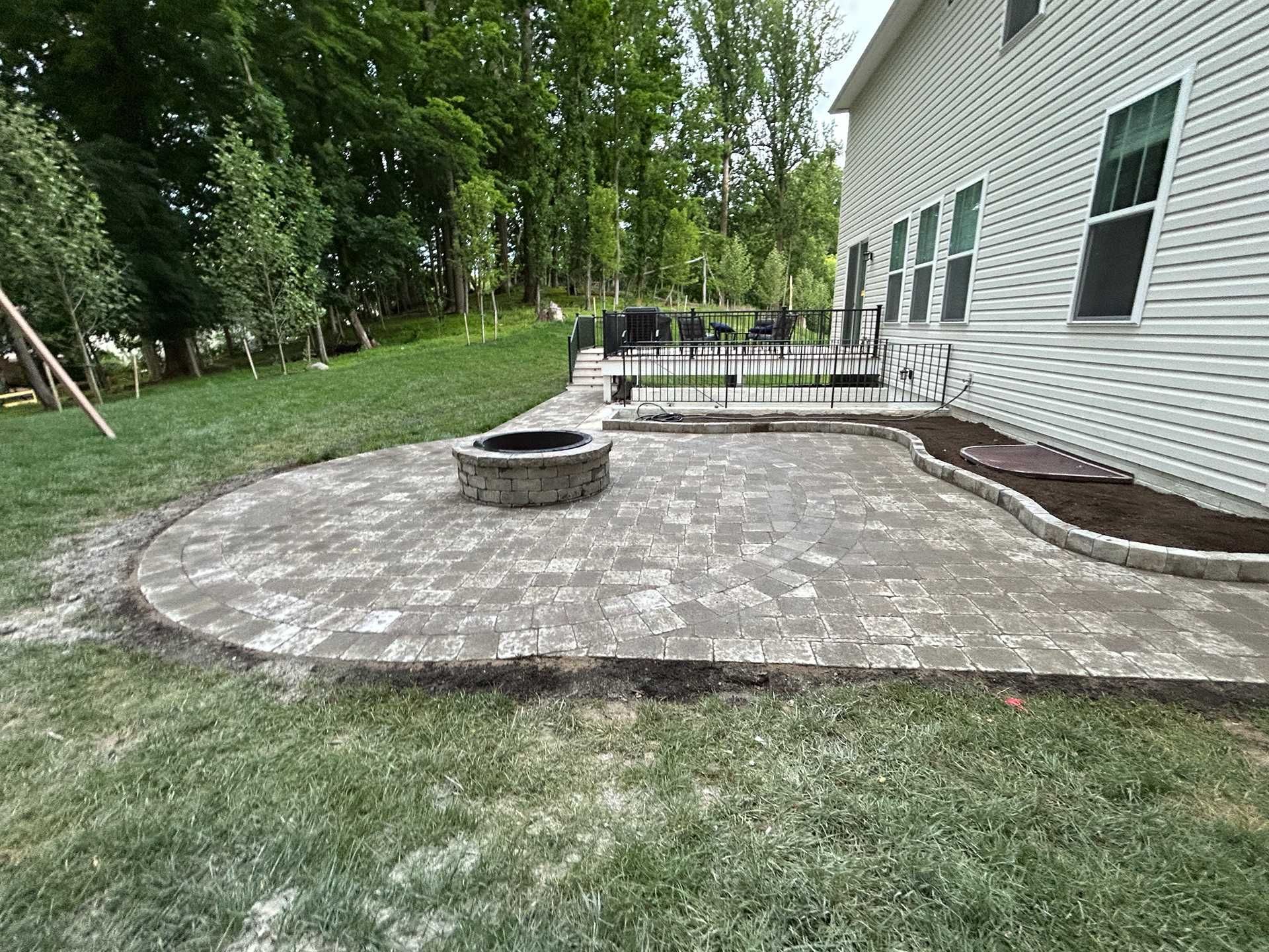 Brick patio with fire pit, bordering lawn. House with windows visible in the background.