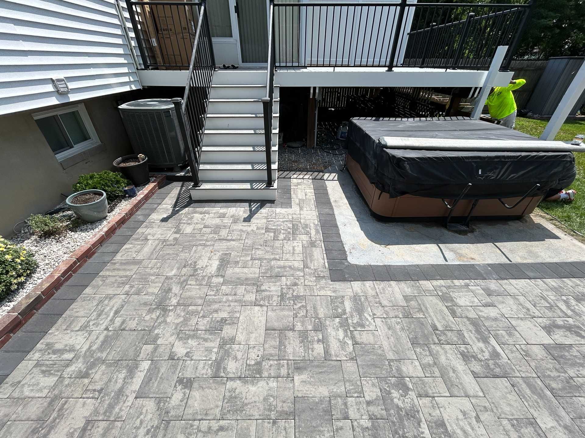Gray paver patio with stairs to a deck, and hot tub.