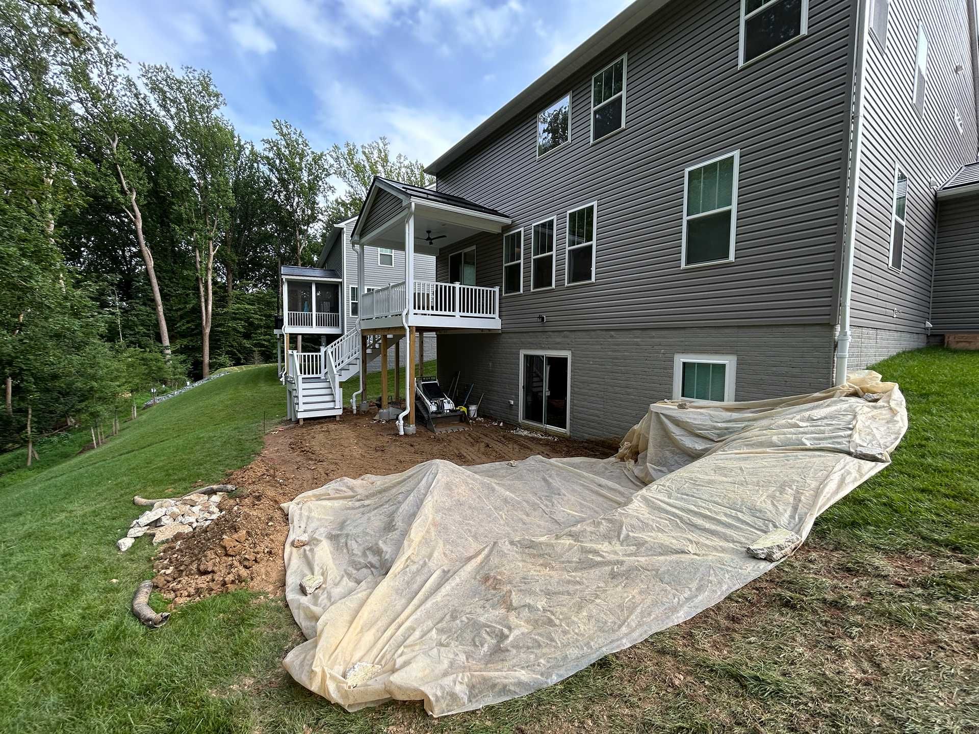 A house exterior with a deck, showing soil preparation for landscaping on a sloped yard.