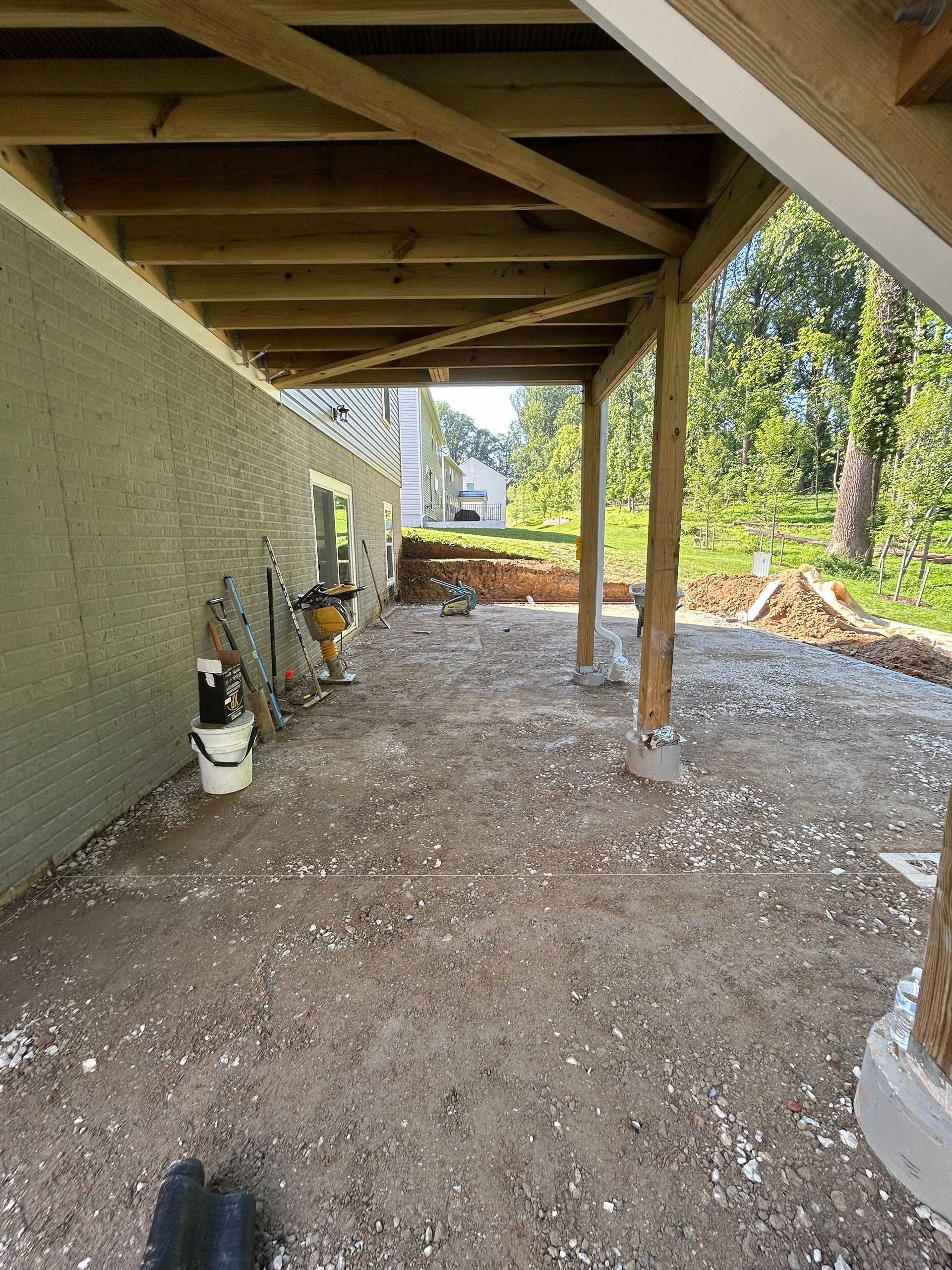Underneath a wooden deck, a gravel-covered area next to a stucco wall; wooden support beams visible.