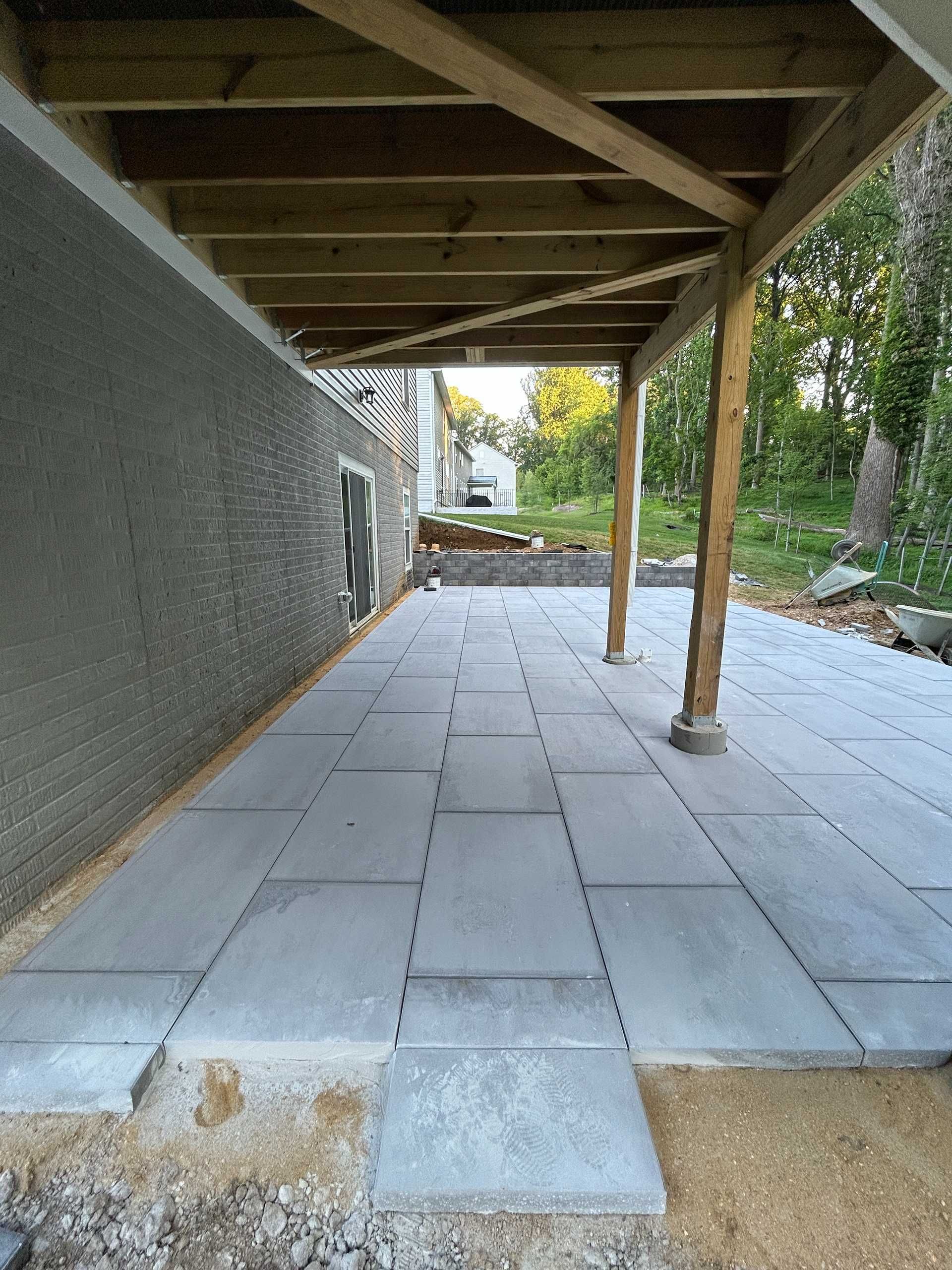 New stone patio under a wooden porch roof, next to a gray stucco wall.
